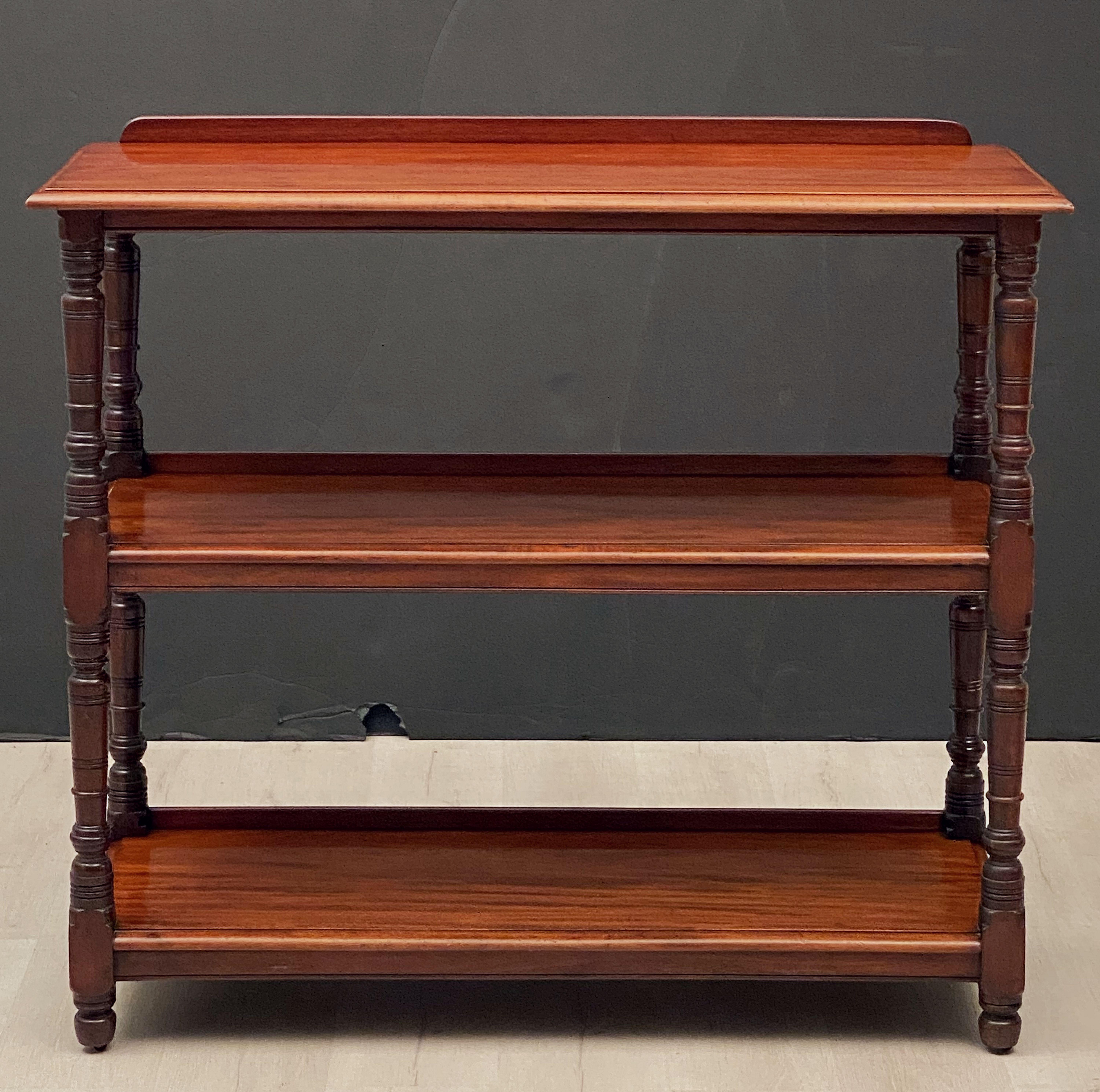 A fine English buffet trolley or console server (or dumb waiter) of mahogany, featuring three tiers with edge-moulded tops, each with back gallery frieze, each tier adjoined to four turned column supports, set upon rolling brass casters.

Engraved