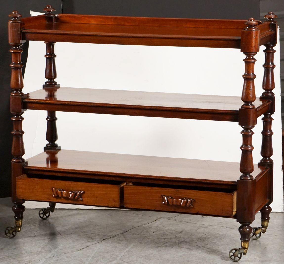 A fine English trolley server (or dumb waiter) of mahogany featuring three tiers with mouded-edge tops, each tier adjoined to four turned column supports, set upon rolling spoke casters of brass. 
The top tier with gallery around the sides and