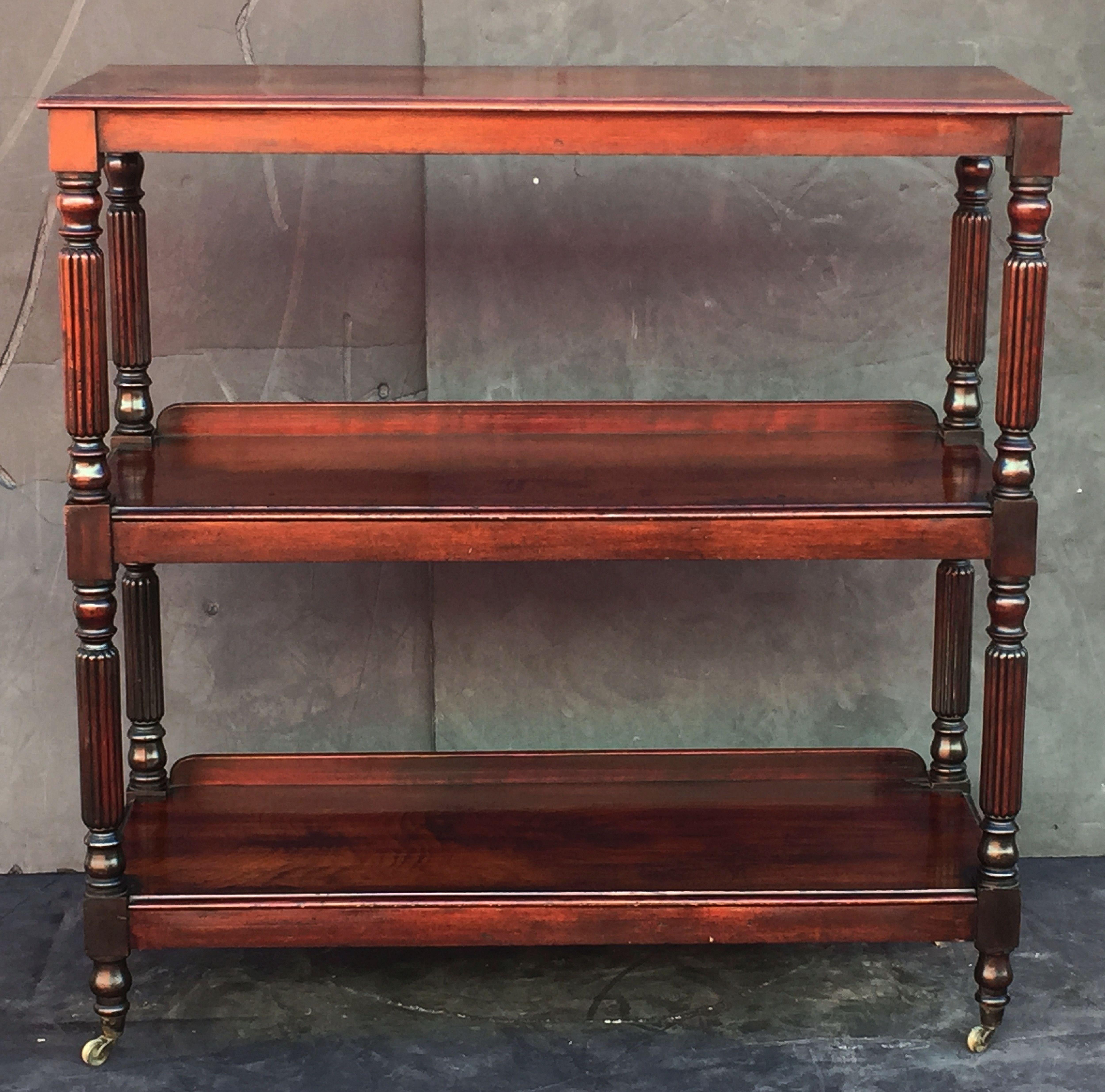 A fine English trolley server (or dumb waiter) of mahogany featuring three tiers with edge-moulded tops, with William IV styling, each tier adjoined to four turned column supports, set upon rolling brass casters.

Such servers (often referred to