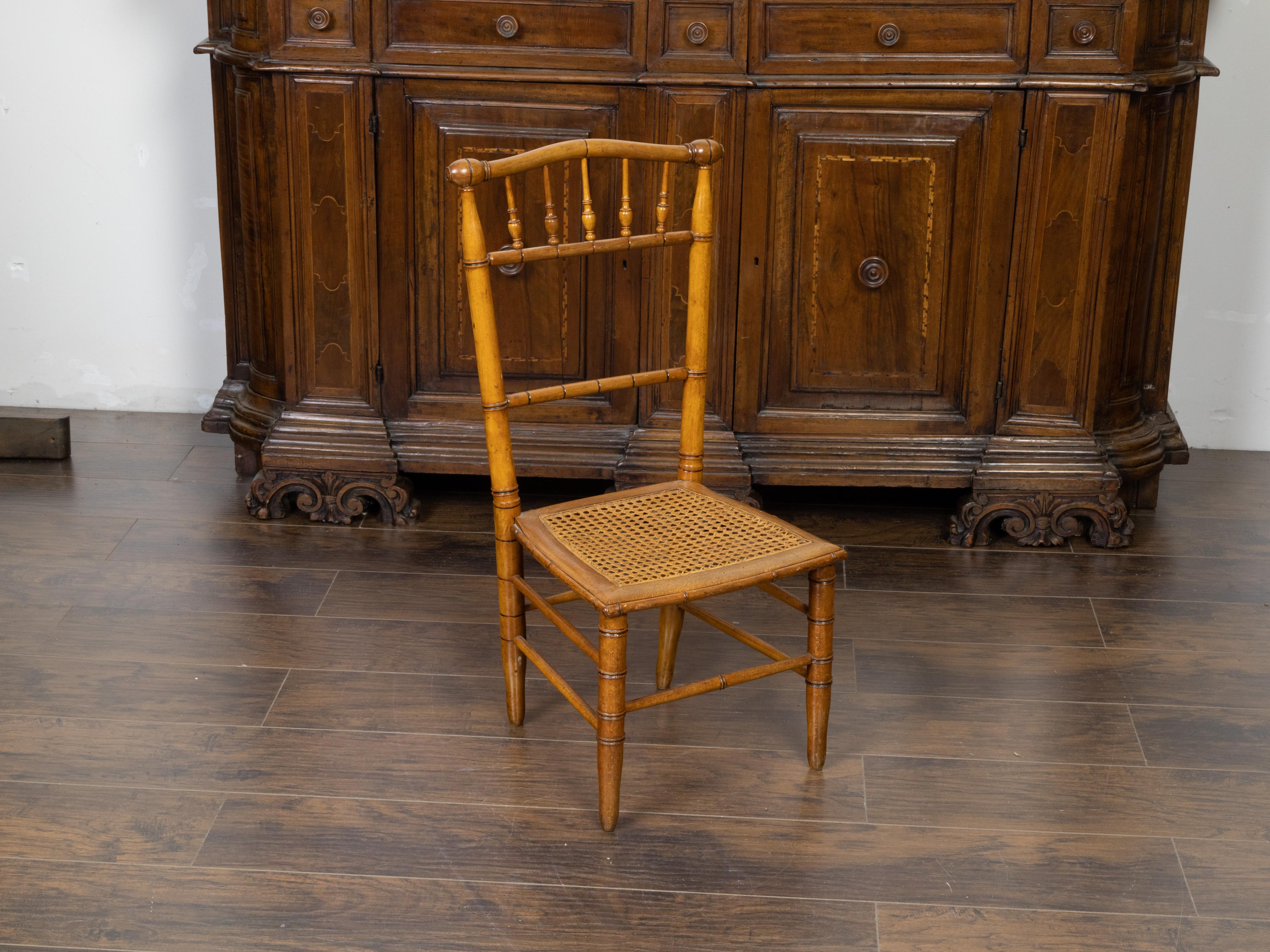 An English Turn of the Century bamboo slipper chair from the early 20th century, with cane seat. Created in England during the early years of the 20th century, this bamboo slipper chair features a spindle back with curving upper rail, sitting on a