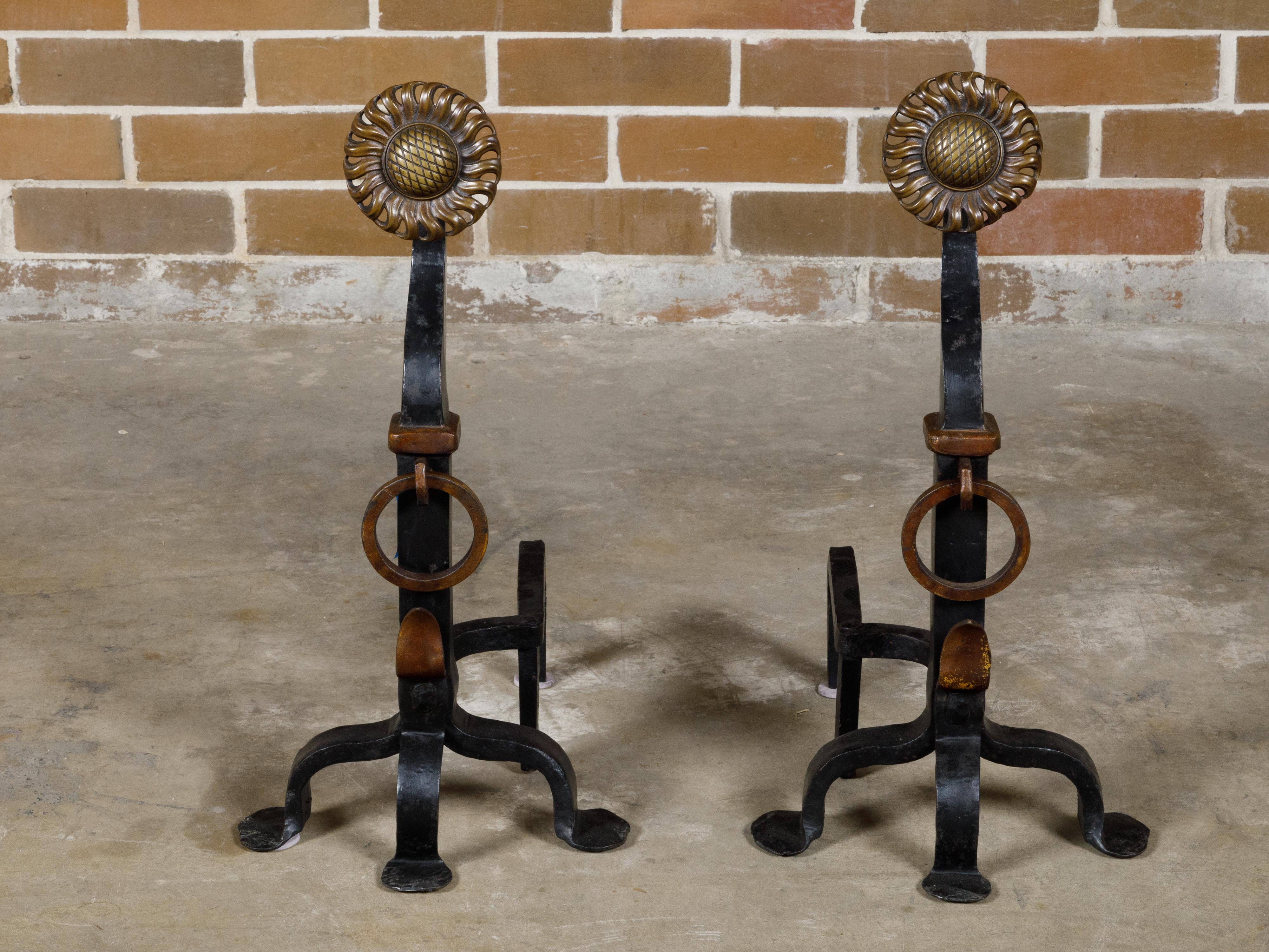 A pair of English Turn of the Century iron and brass sunflower andirons from circa 1900 with three scrolling legs. Embrace the charm and craftsmanship of yesteryears with this exquisite pair of English iron and brass andirons, adorned with sunflower