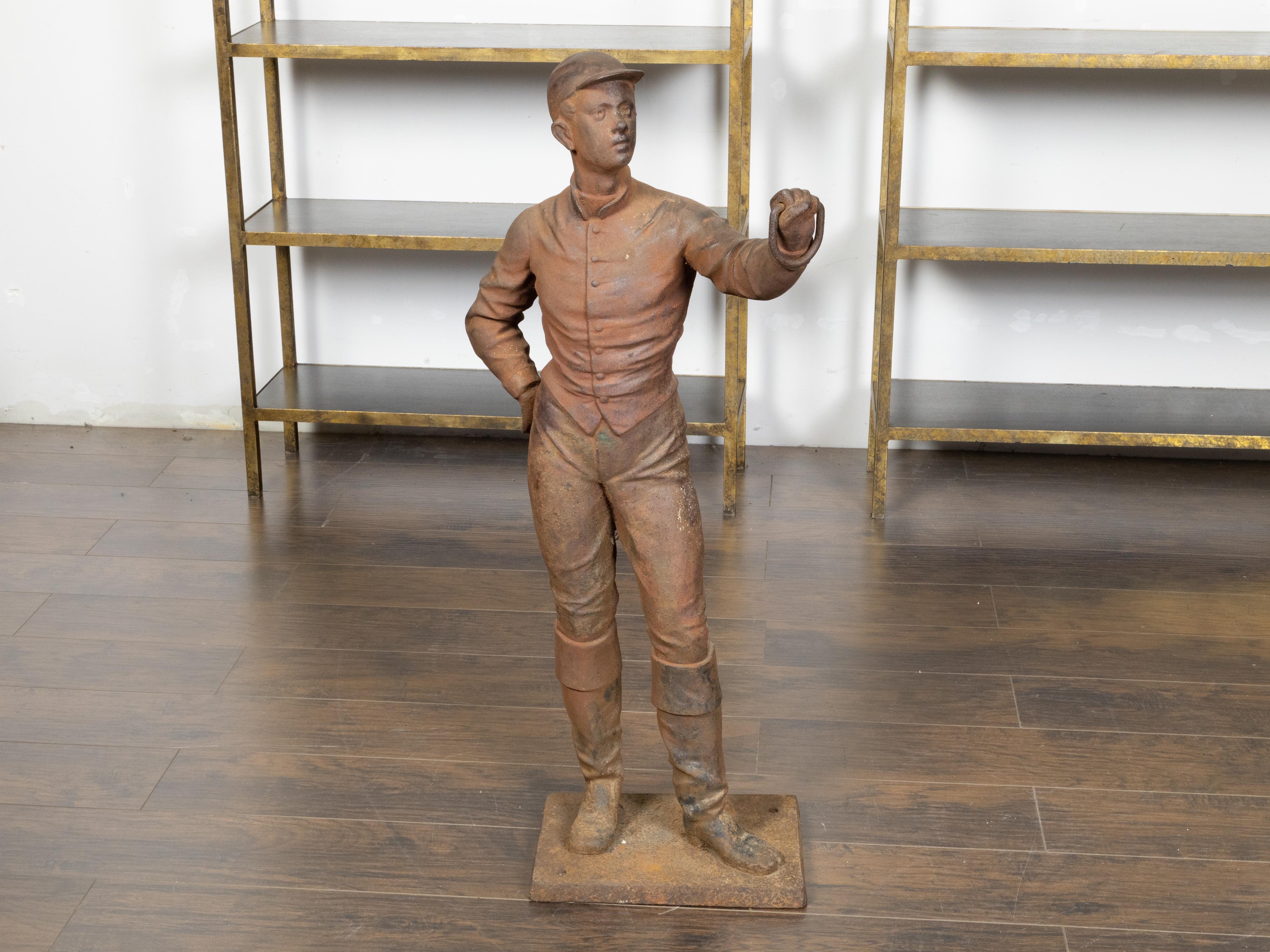 An English Turn of the Century iron sculpture depicting a jockey holding a ring in his left hand. Created in England during the Turn of the Century which saw the transition between the 19th to the 20th century, this iron sculpture depicts a male