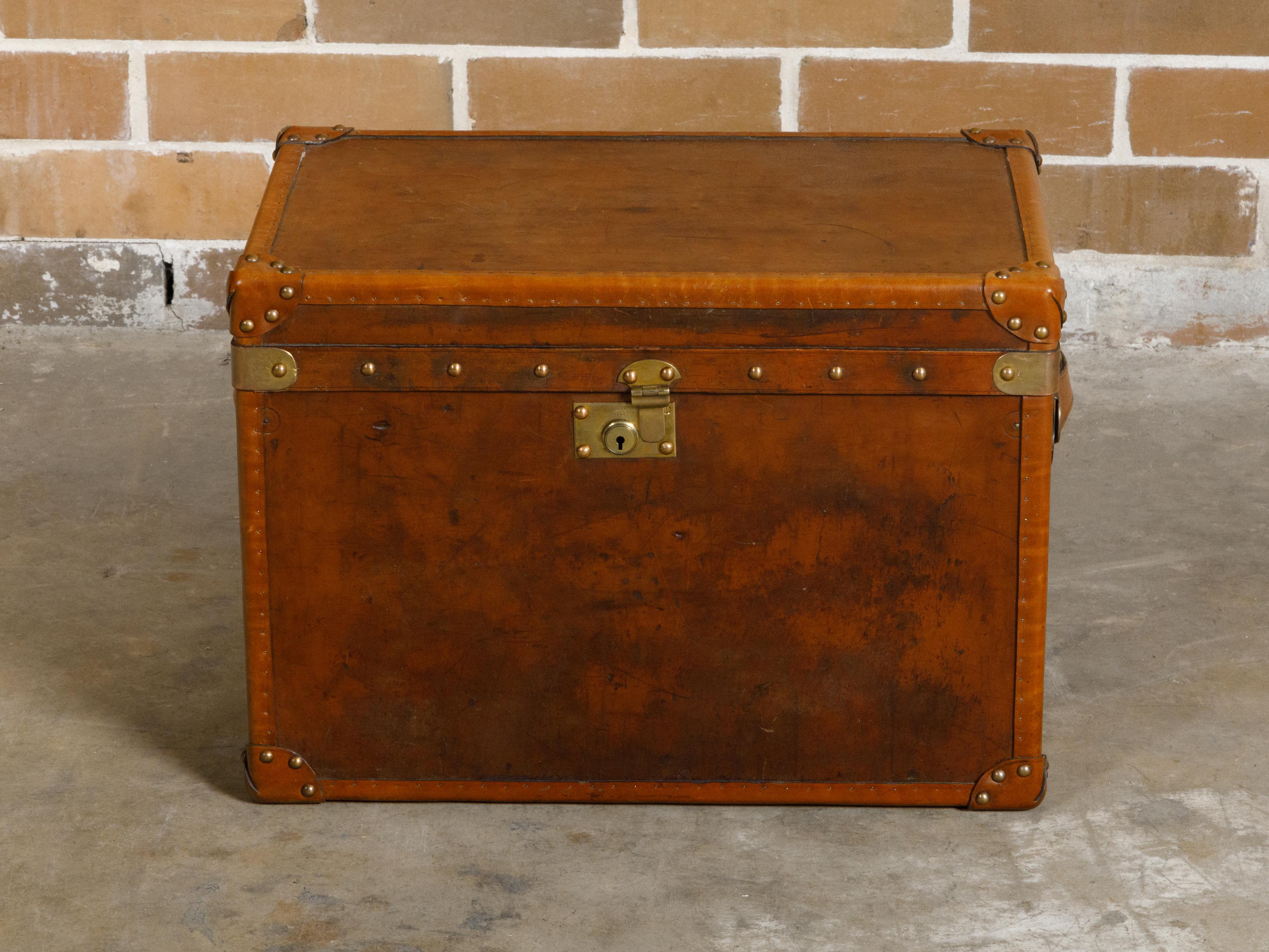 An English Turn of the Century leather trunk from circa 1900 with brass accents, lateral handles and monogram. This English Turn of the Century leather trunk, dating back to circa 1900, presents a remarkable blend of vintage allure and timeless
