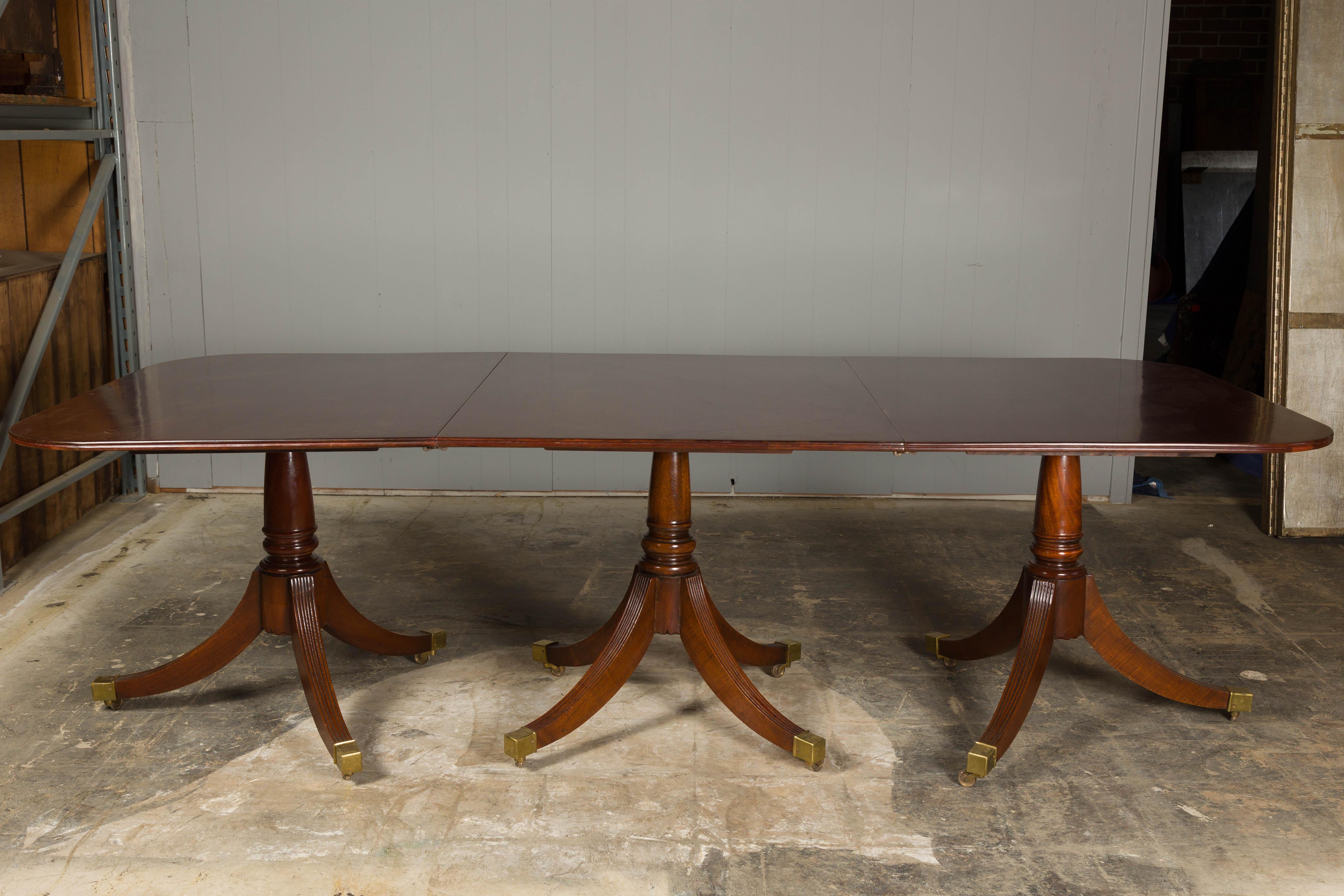 An English Turn of the century mahogany extension dining room table circa 1900 with two removable leaves and three quadripod bases. Step into a realm of grace and timeless elegance with this exquisite English Turn of the Century mahogany extension