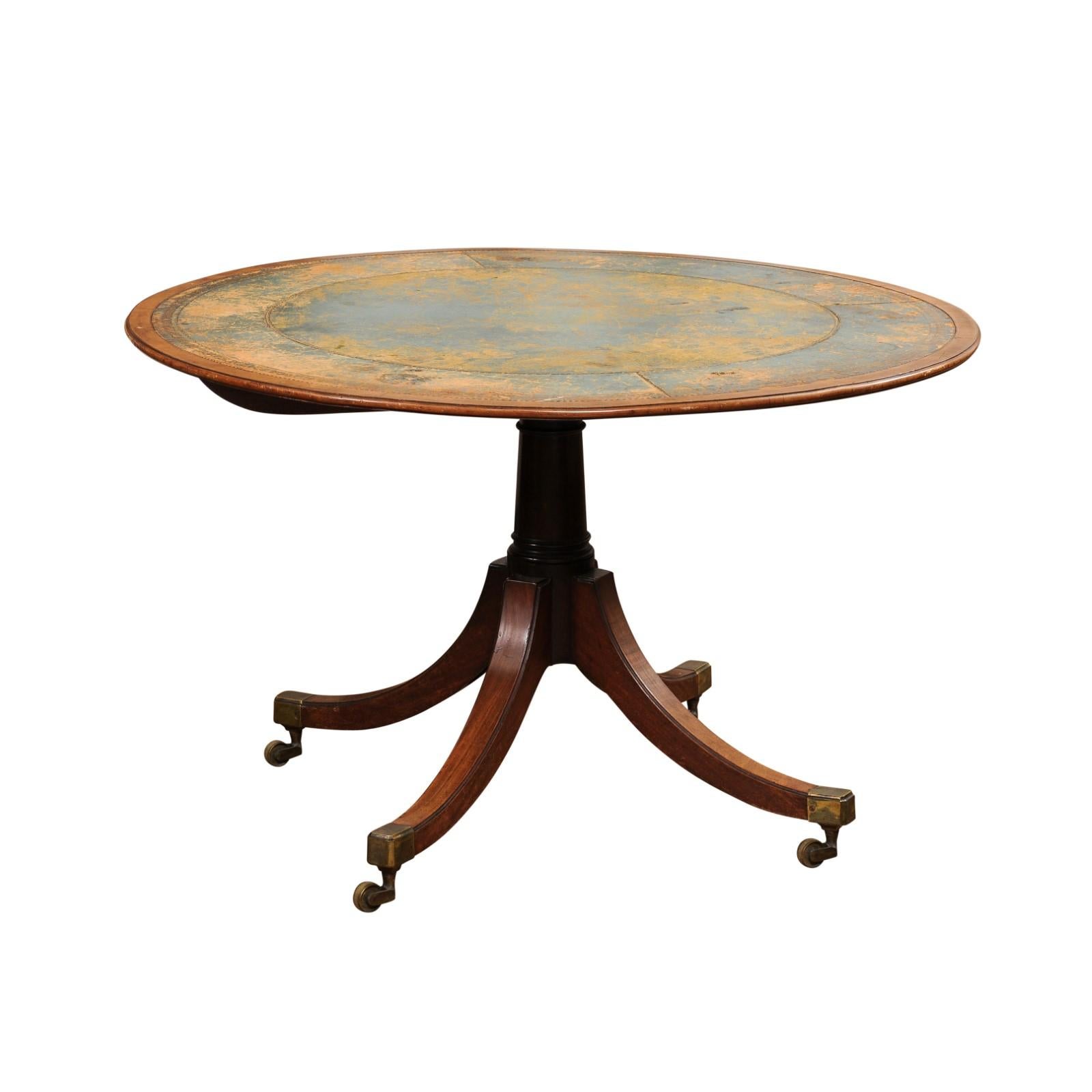 An English Turn of the Century mahogany and leather tilt top centre table with quadripod base and casters. Step into the allure of a bygone era with this exquisite Turn of the Century English tilt-top table, a piece that marries the rich warmth of