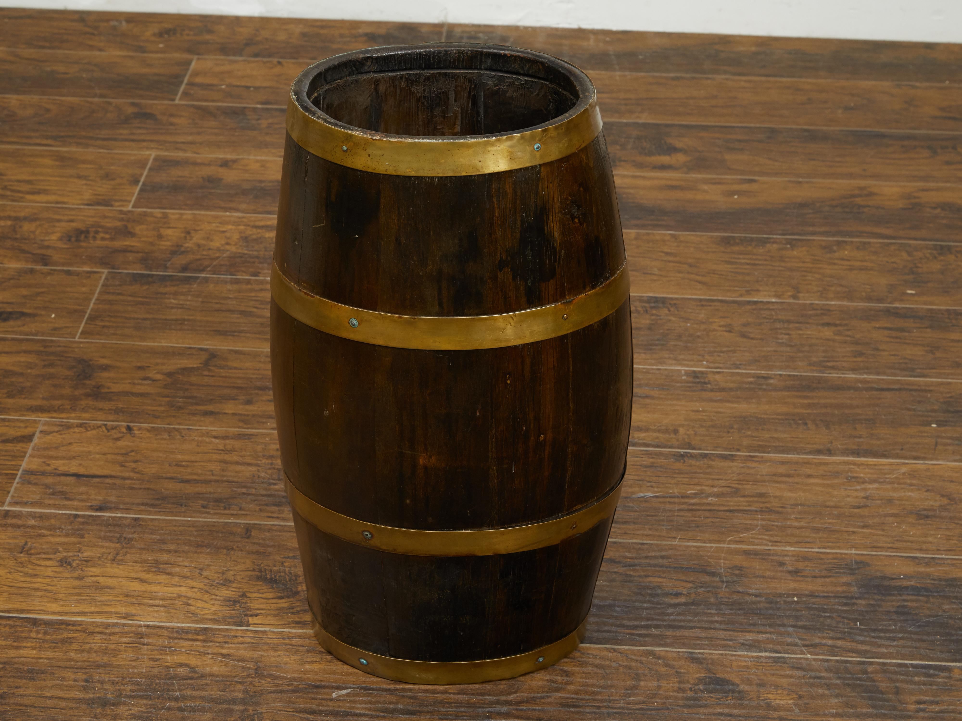 An English turn of the century oak barrel from the early 20th century, with brass braces. Created in England during the early years of the 20th century, this barrel features a sturdy oak body made vertical slats contrasted by the golden tones of the