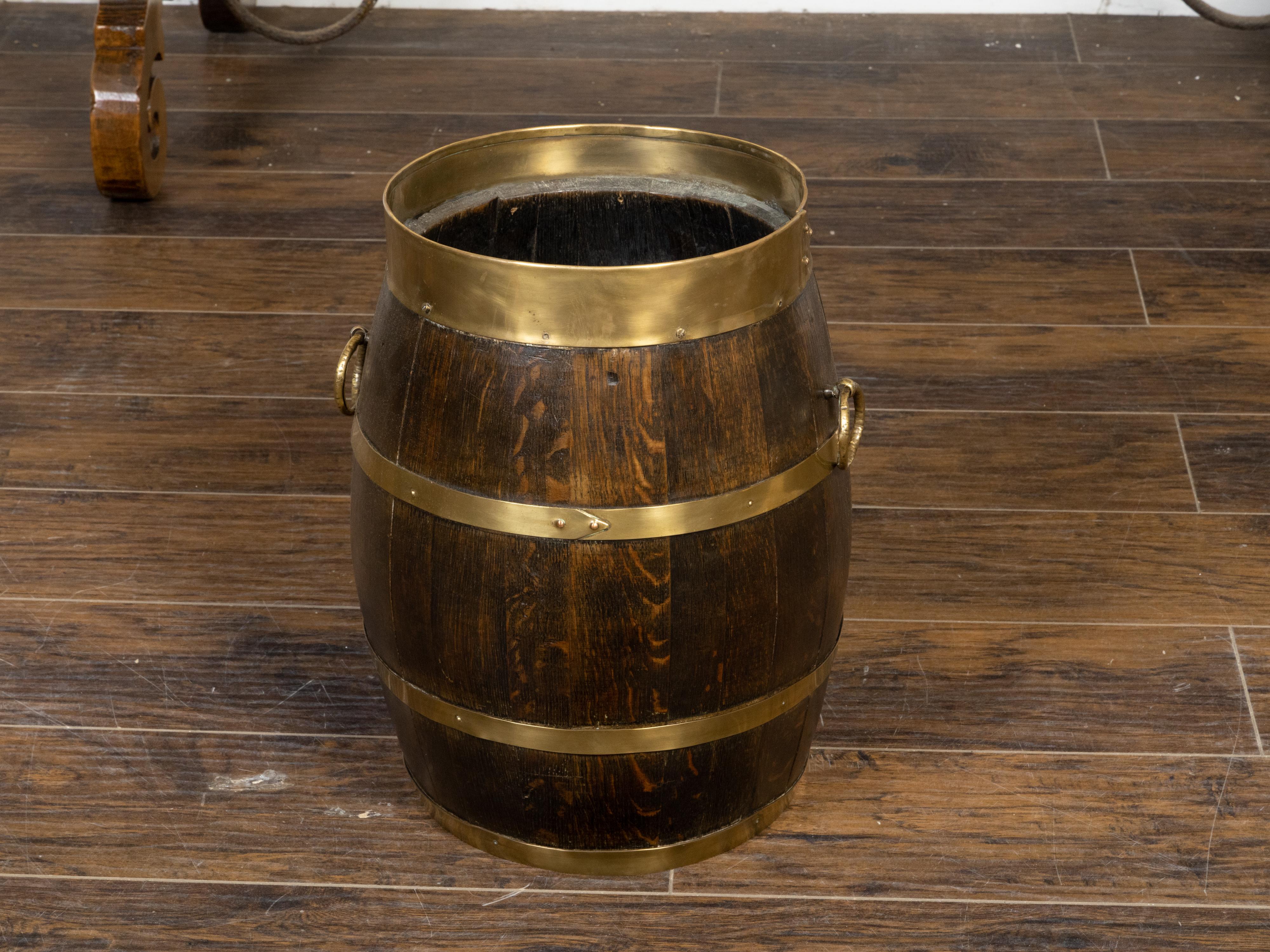 A rustic English turn of the century oak barrel from the early 20th century, with brass braces, and ring handles. Created in England during the Turn of the Century which saw the transition between the 19th to the 20th century, this barrel features a