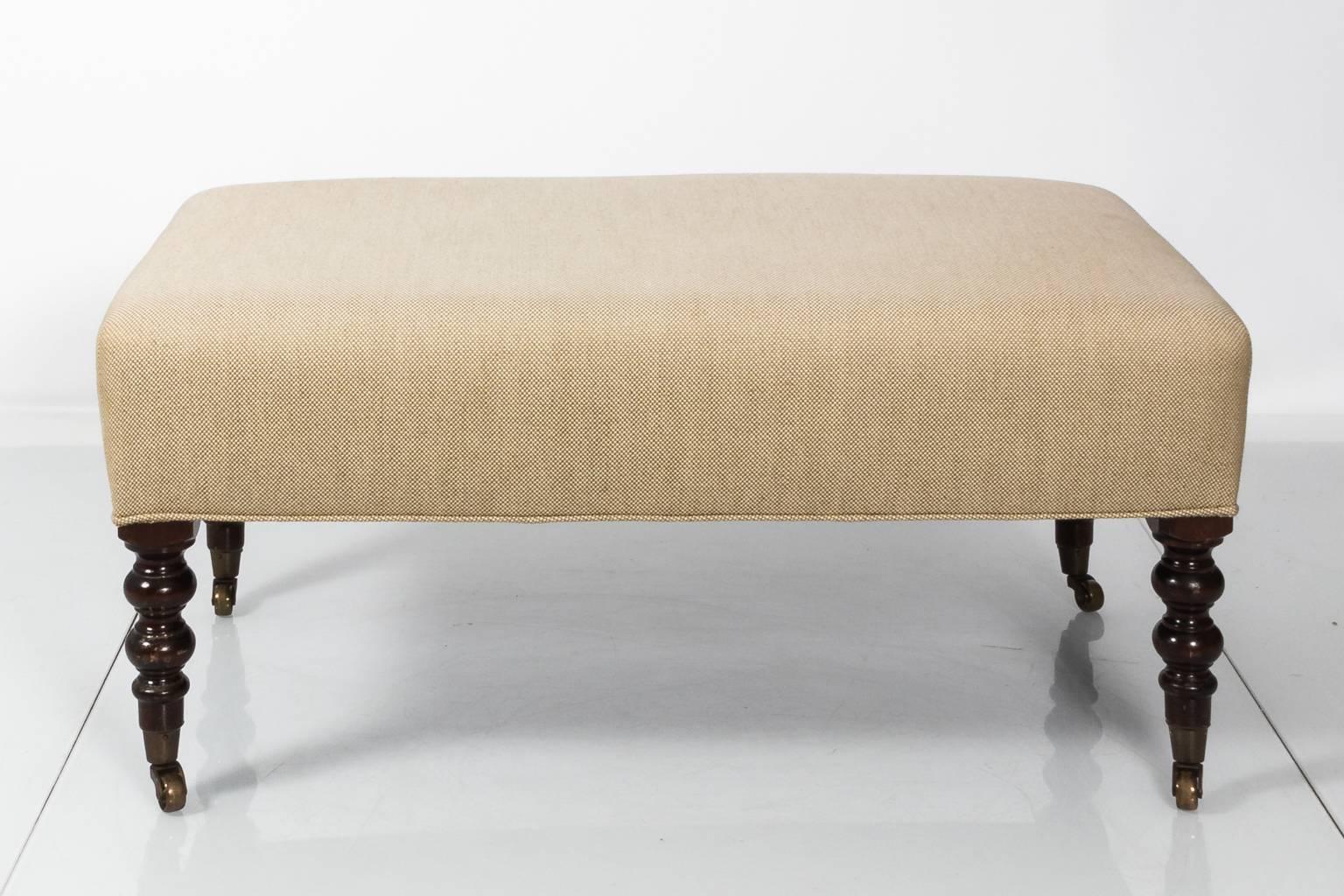 English upholstered bench with ball turned legs on brass castors, circa late 20th century.
   