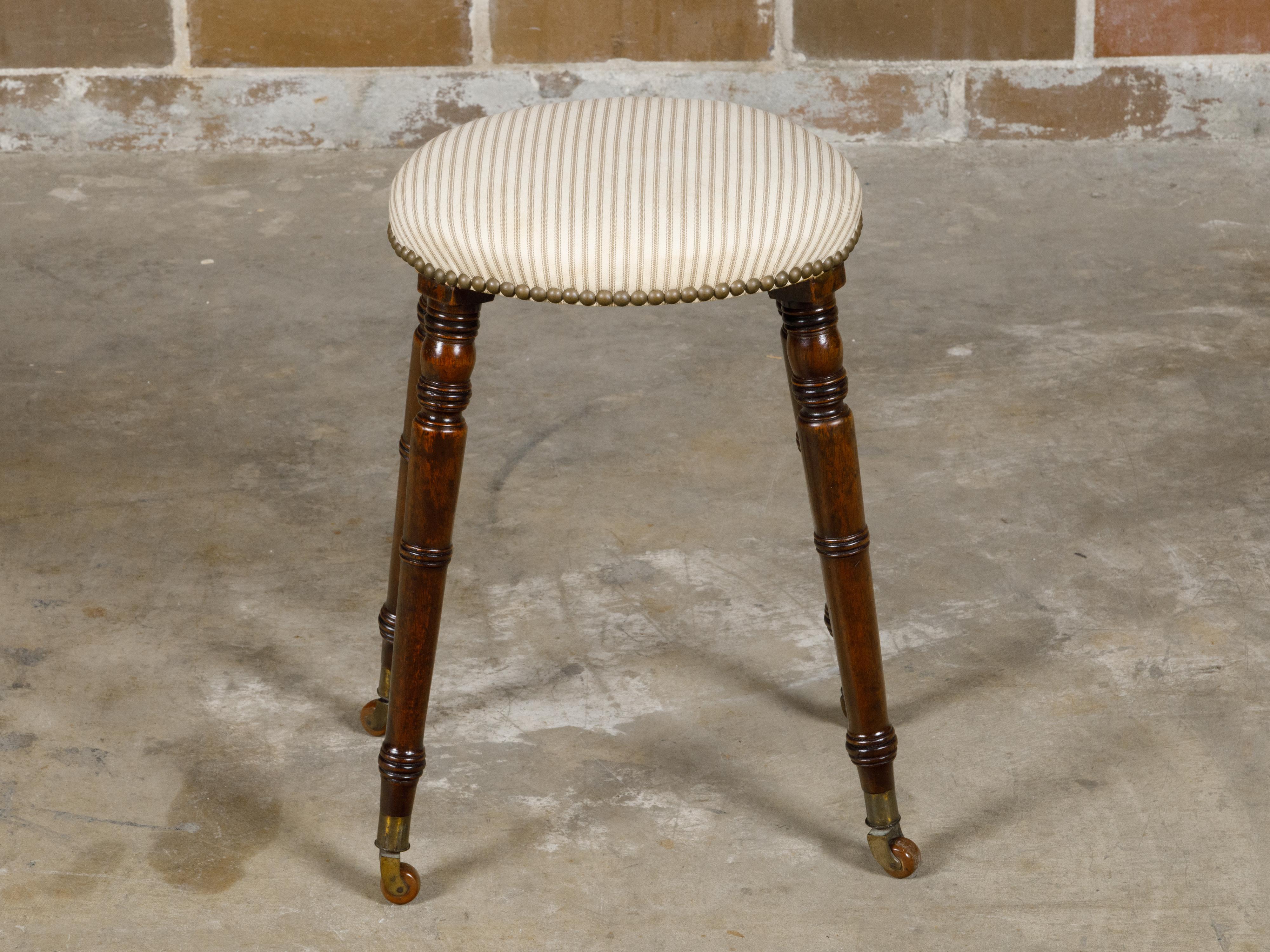 An English Victorian period oak stool from the 19th century with oval upholstered seat, turned legs resting on casters. Step into the charm and craftsmanship of the 19th century with this English Victorian period oak stool, a piece that beautifully