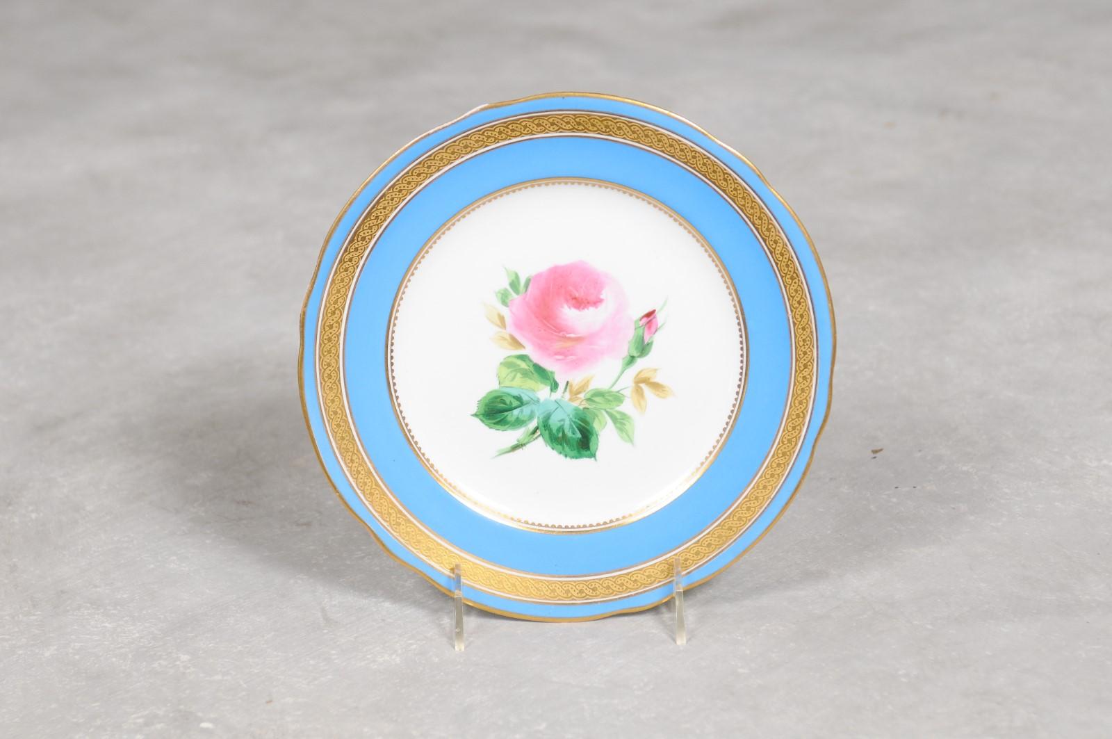 An English turquoise and white faience dessert plate from the 19th century, with painted pink rose and gilt border. Created in England during the 19th century, this dessert plate features a turquoise border accented with a gilt trim, surrounding a