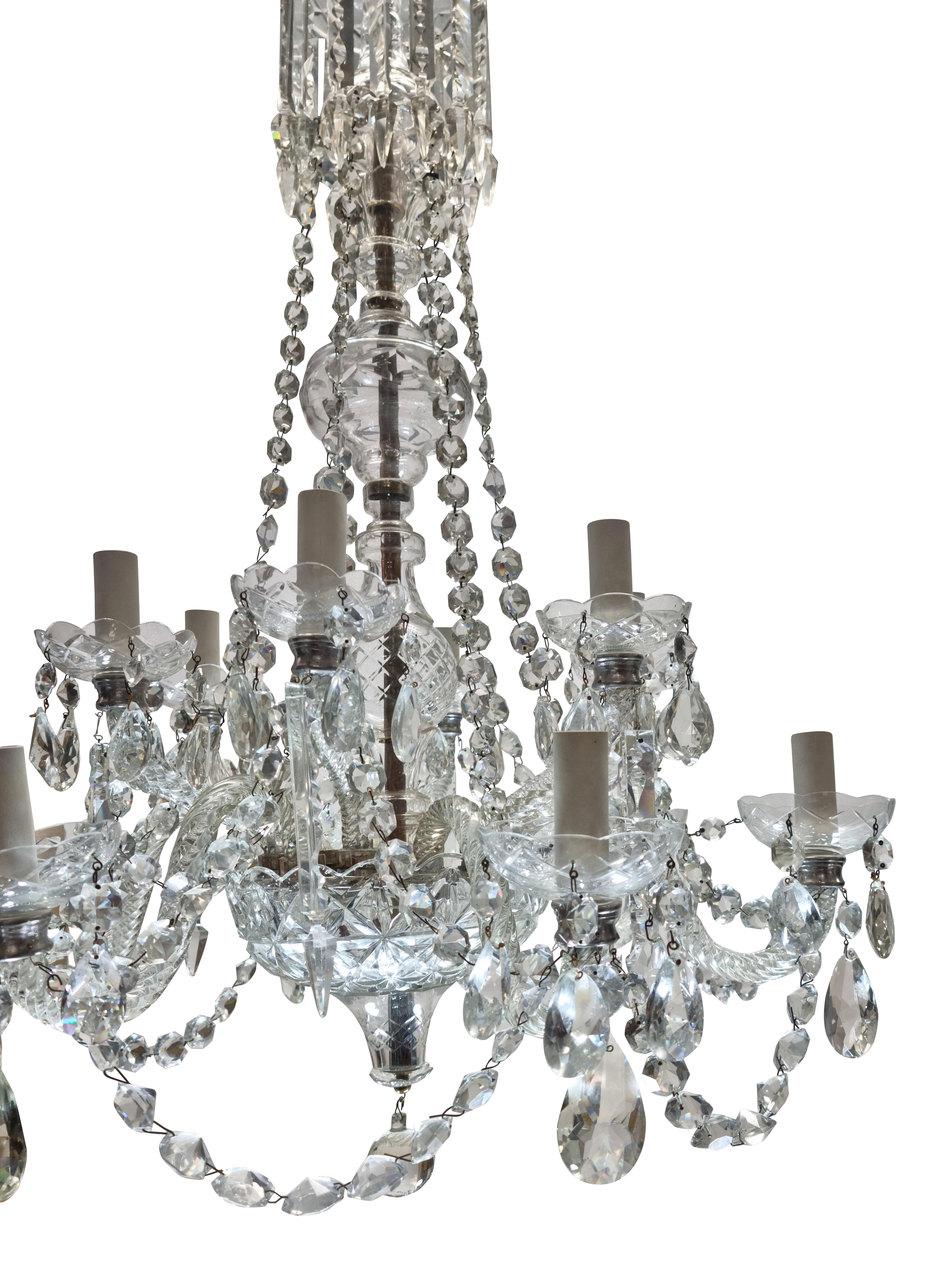 An English cut glass chandelier of twelve lights, hung throughout with finely cut swags, pendants and prisms. The central baluster and receiver dish, profusely cut.