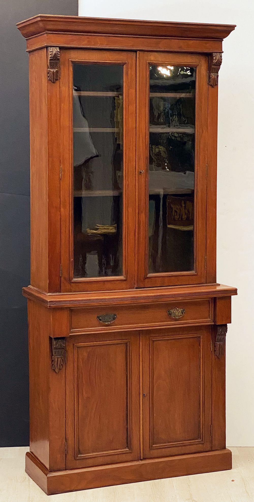 A fine English two-tied bookcase cabinet of mahogany from the 19th century, featuring an upper tier with crown moulding over two glazed doors, opening to three shelves of adjustable height. 
Mounted to a bottom tier showing a frieze of one long