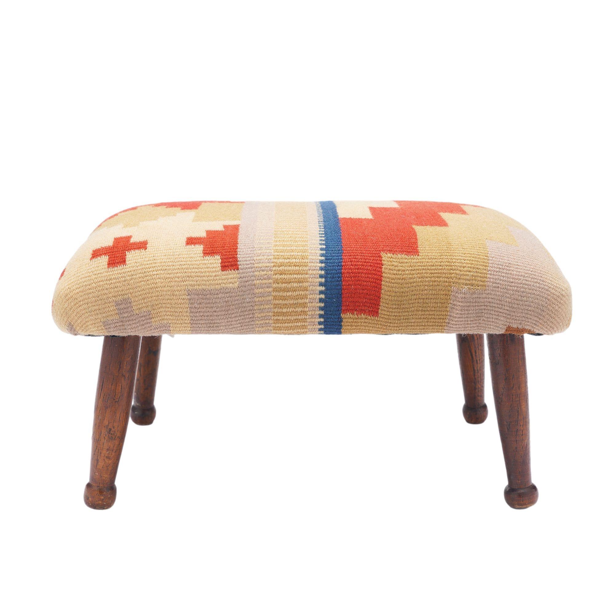 Rechteckiger Fußhocker auf gedrechselten Eichenbeinen, die in Knopffüßen enden. Die Oberseite des Hockers ist mit einem handgewebten Wollkelim-Fragment mit geometrischem Muster gepolstert.

England, ca. 1850-1900.