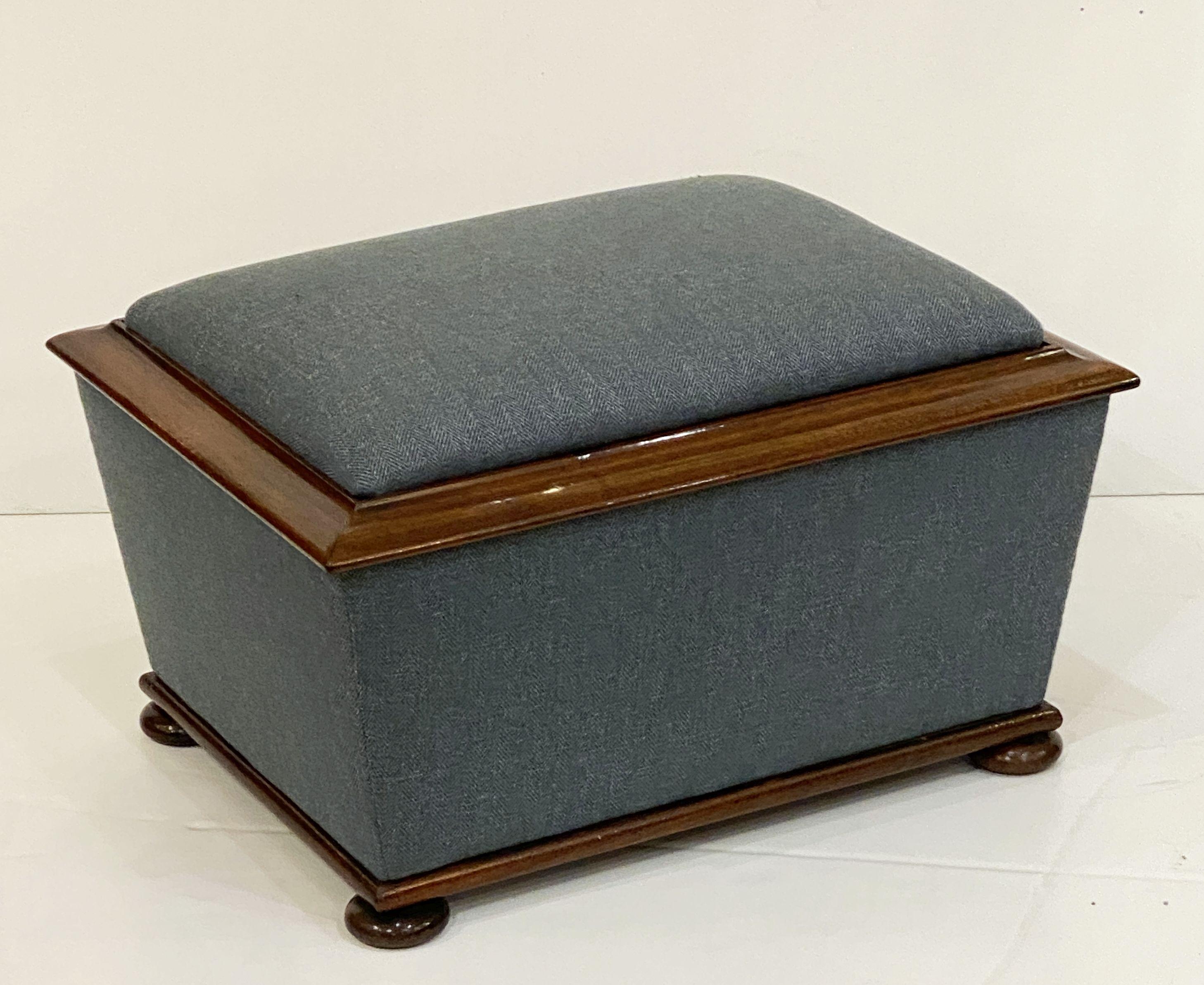 A handsome, comfortable English rectangular upholstered trunk or frame ottoman (pouffe), featuring an upholstered seat with hinged, tufted lid that lifts for storage, framed with accents of mahogany around the top and base, and resting on bun feet.