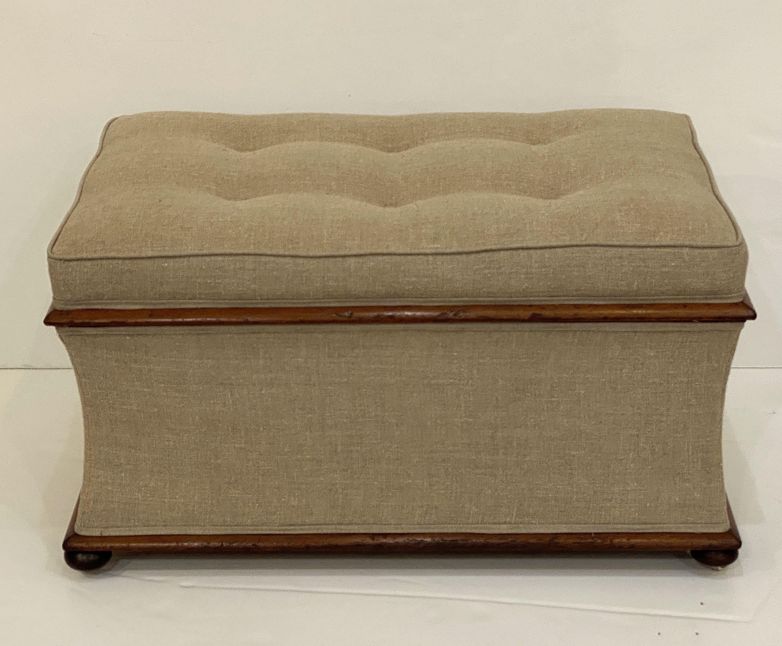 A handsome, comfortable English rectangular upholstered trunk or pouffe ottoman, featuring an upholstered seat with hinged, tufted lid that lifts for storage, framed with accents of mahogany around the top and base, and resting on bun feet with