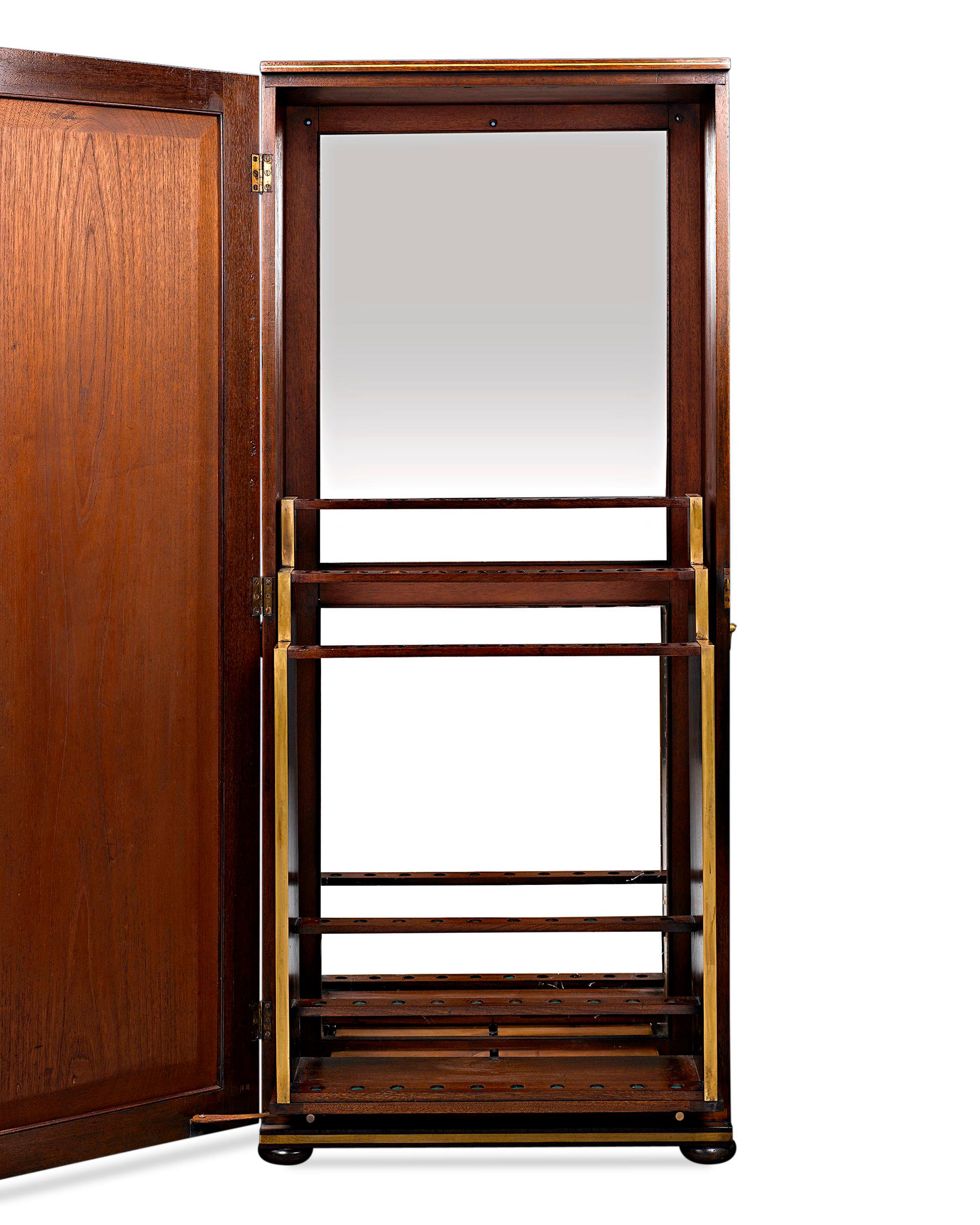 This English cane cabinet exhibits classical style and impeccable design. Crafted of lustrous Cuban mahogany, this upright case features a beautifully paneled door which opens to reveal a three-tiered cane rack for 30 walking sticks. This ingenious