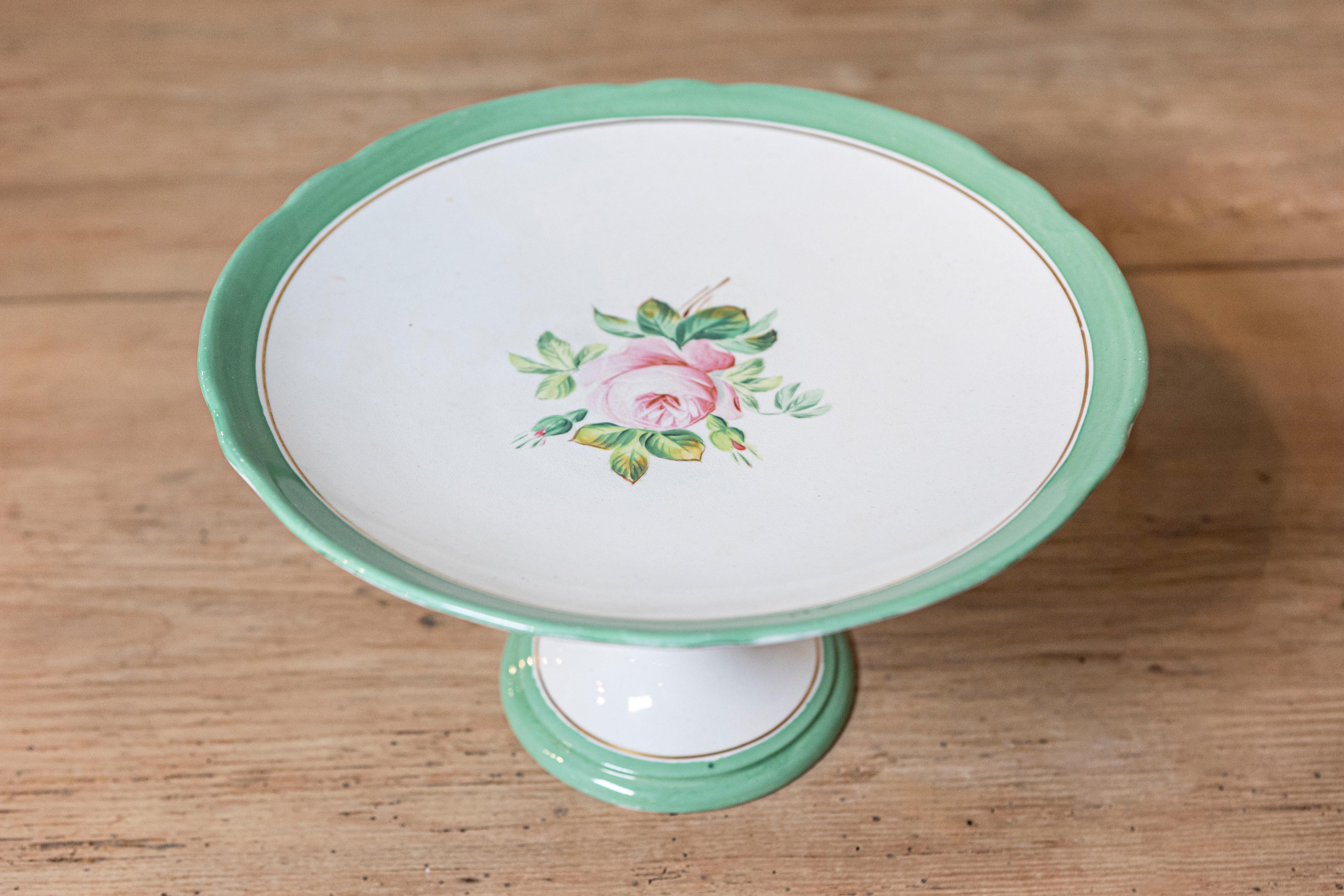An English Victorian botanical compote from the late 19th century, with pink roses, green and gold trim and hourglass-shaped base. Born in England during Queen Victoria's later years, this charming compote features a delicate central rose surrounded