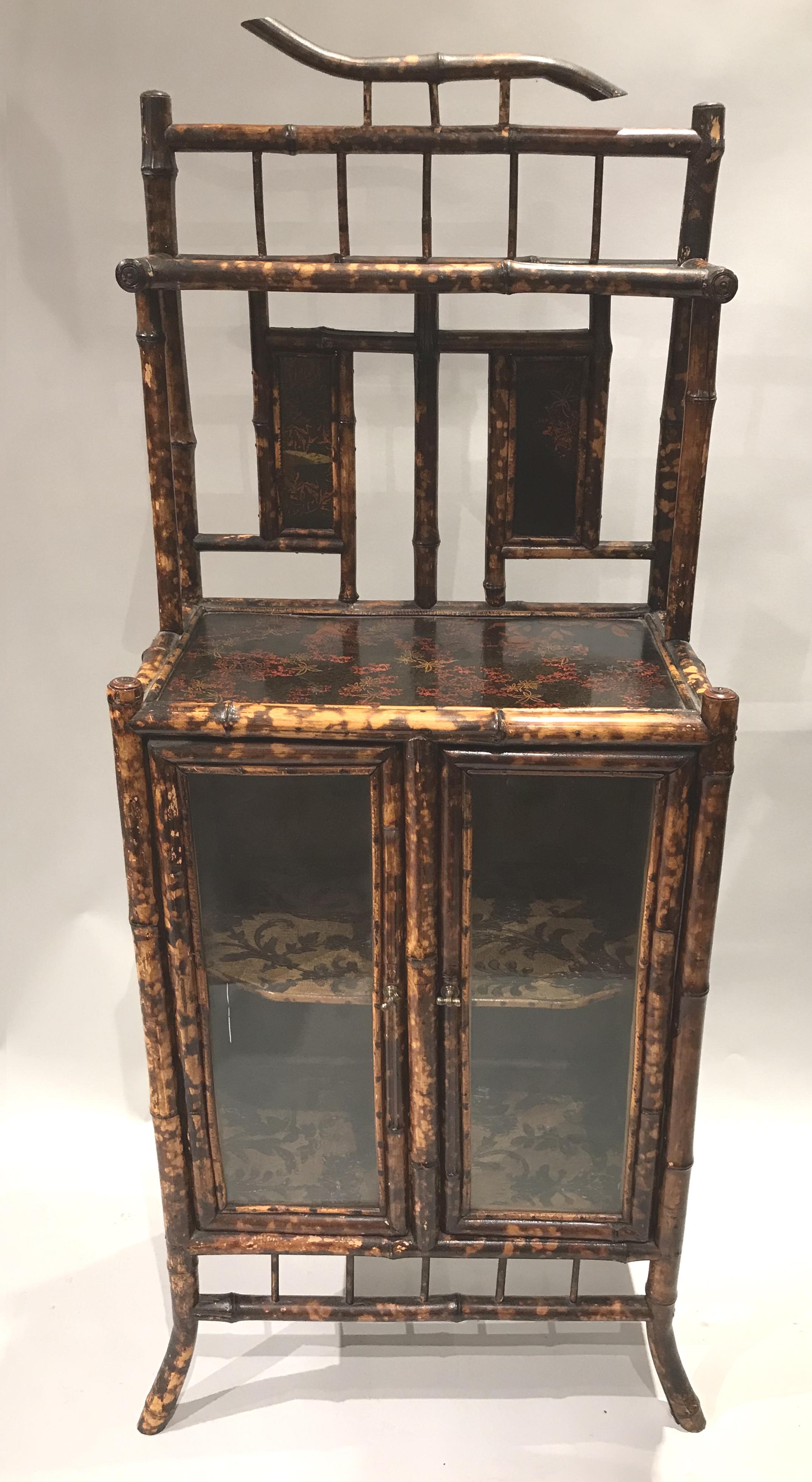 A fine English Victorian bamboo cabinet or etagere with foliate decorated shelves and two glass doors which open to a foliate paper lined one shelf interior compartment. Very good condition, with minor losses and restorations, as well as light