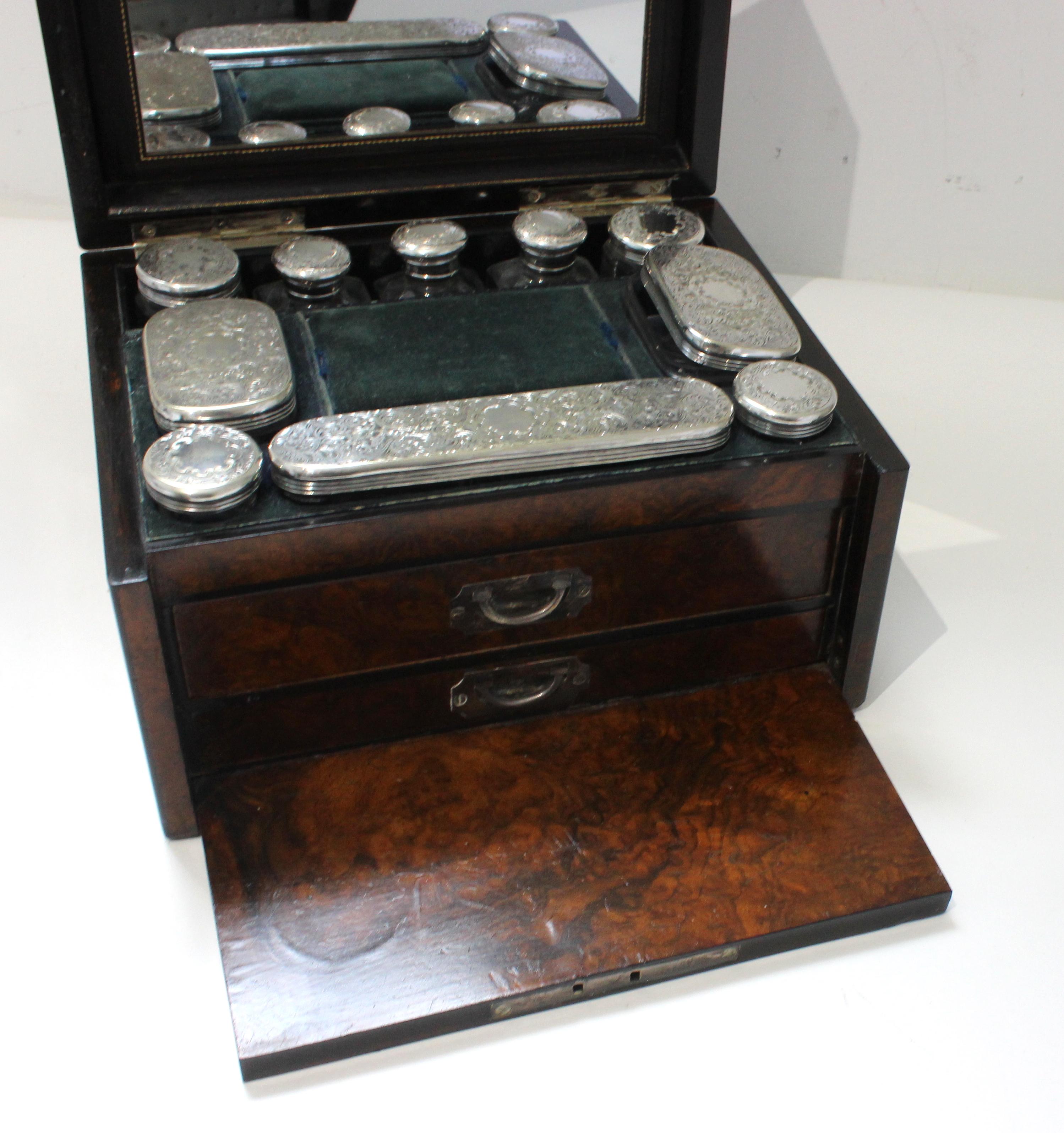 This stylish and chic English traveling case dates to the 19th century, and the piece is fabricated in velvet, burlwood, ebony and brass. The case interior holds ten storage pieces, which are fabricated in cut glass and silverplated tops. 

Note: