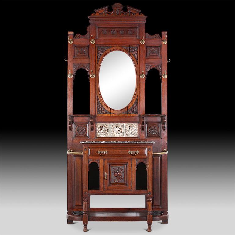 English Victorian carved mahogany hall stand with tiles and the original brass hooks. Featuring an oval bevelled mirror and a marble surface, and with a small drawer above a cabinet. C.1890