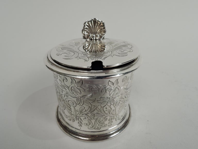 Victorian Classical sterling silver mustard pot. Made by Charles Thomas Fox & George Fox in London in 1858. Drum-form with straight and inset sides, and open bottom. Cover flat and hinged, and scroll-bracket handle with scallop shell thumb rest.