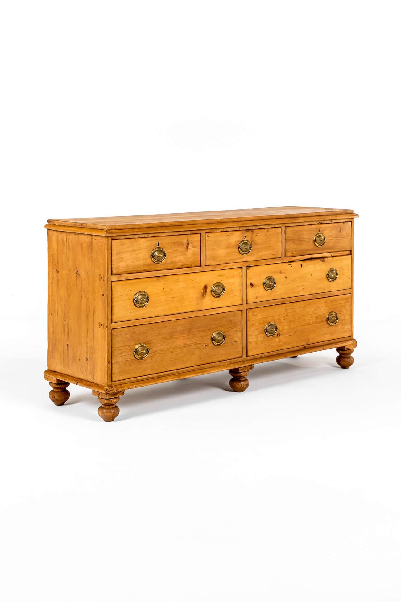 A wonderful country house pine dresser base with a moulded plank top over seven drawers. A configuration of three smaller drawers below four deep and wide smooth running drawers each fitted with cast brass oval drop handles.

The dresser is raised