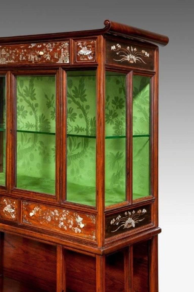 This very fine rosewood cabinet has a glazed upper section with two doors and disguised frieze drawers both above and below, the lower section with two shaped open shelves, finely inlaid in mother of pearl with floral scenes and a battle scene on