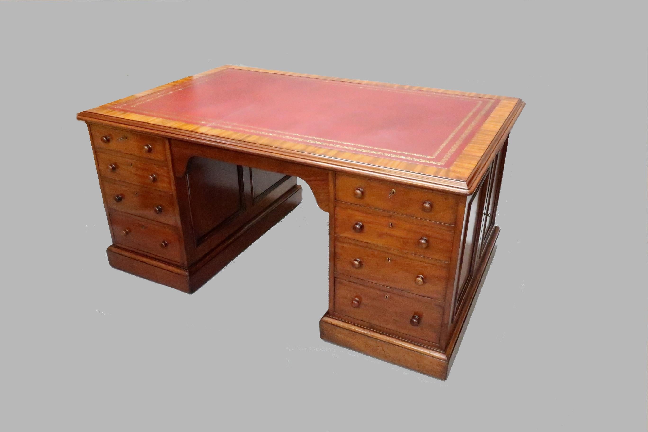 A very good quality Victorian figured mahogany partners pedestal kneehole writing desk with eight drawers to the front and cupboards to the sides. The top has a mahogany crossbanded border with a maroon leather hide finished with gilt tooling and