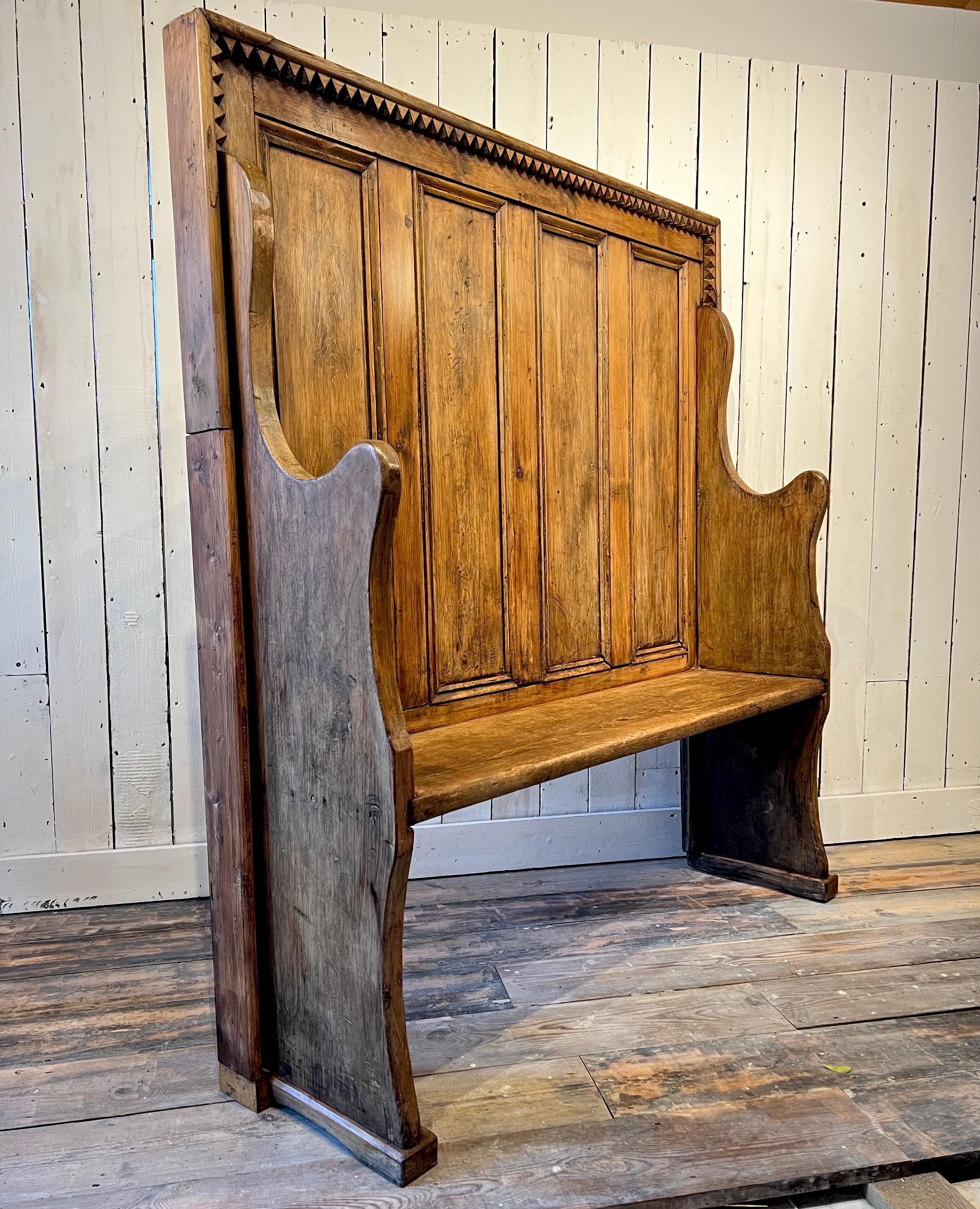 This remarkable 19th Century Victorian Gothic Revival Pine Settle, is a true eye catcher. Its unique dragon teeth motif detail adds a sense of mystery and intrigue to any room or hall. Crafted from pitch pine, this piece boasts a mid Oak finish and
