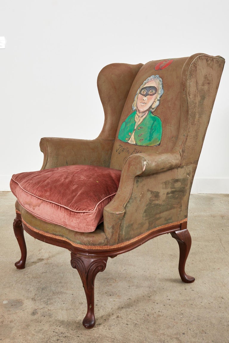 Whimsical 19th century English Victorian wingback armchair featuring painted leather by artist Ira Yeager (American 1938-2022). The chair features a painted bust of a masked gentleman 