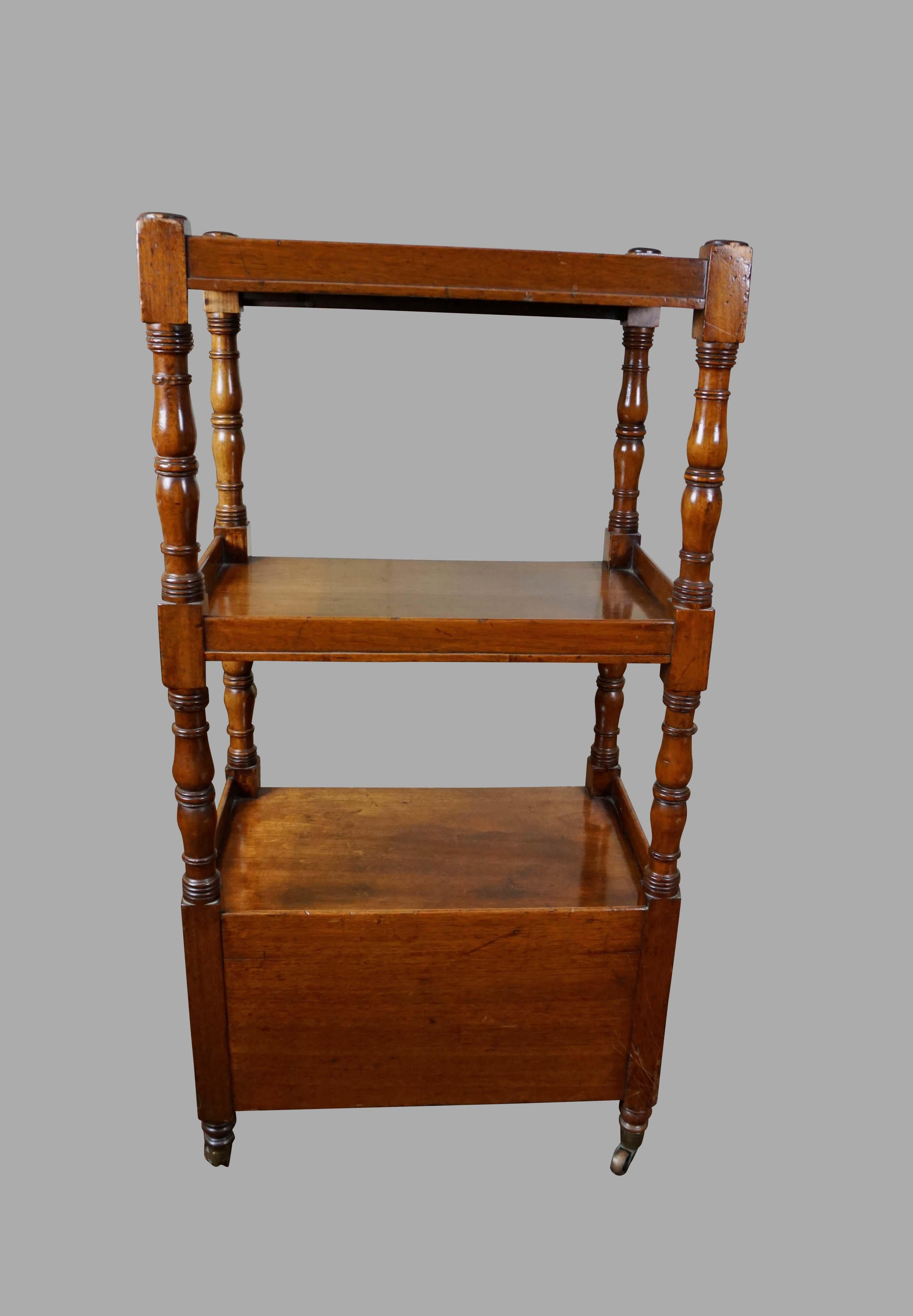 An English Victorian period light mahogany what-not or étagère with turned columns supporting 3 shelves above a pair of drawers resting on legs ending in brass casters, circa 1850-1860.