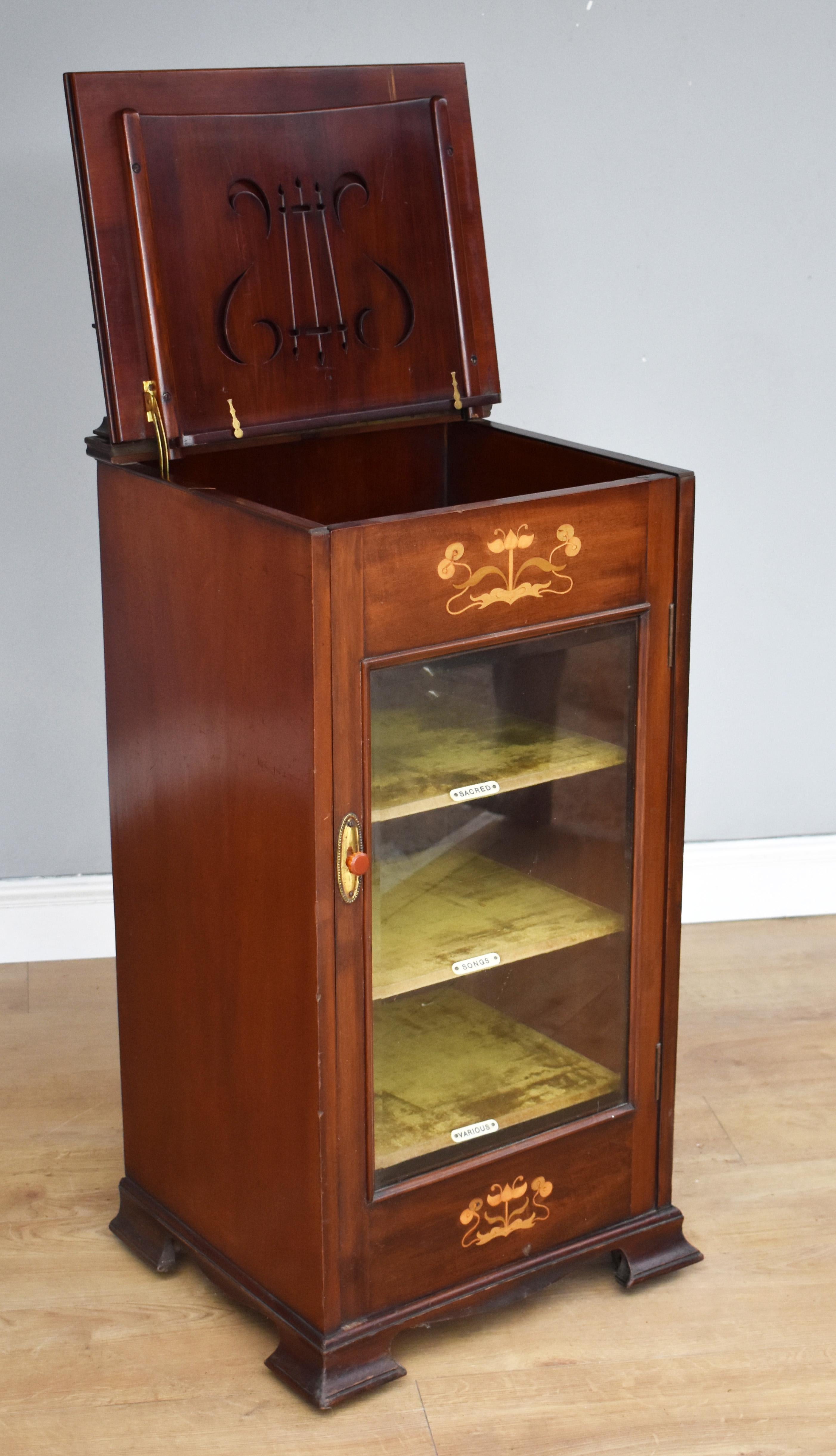 For sale is a good quality Victorian mahogany inlaid Art Nouveau music cabinet, having a raised inlaid gallery above a hinged lid, opening to reveal a lire shaped music holder above storage space. With a single glass door opening to reveal a fabric