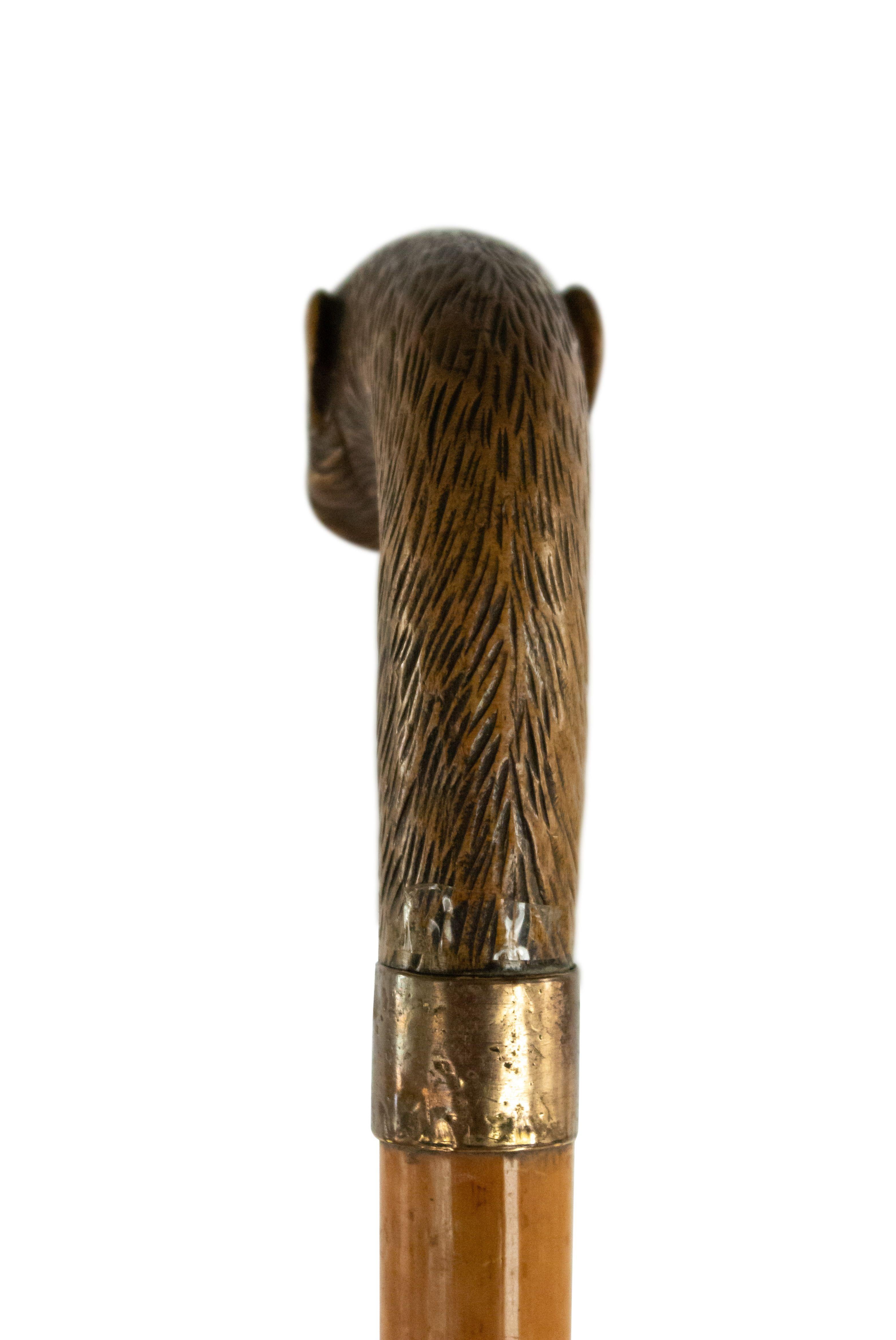English Victorian walking cane with light wood shaft and handle carved as monkey head with metal alloy collar stamped 995.
