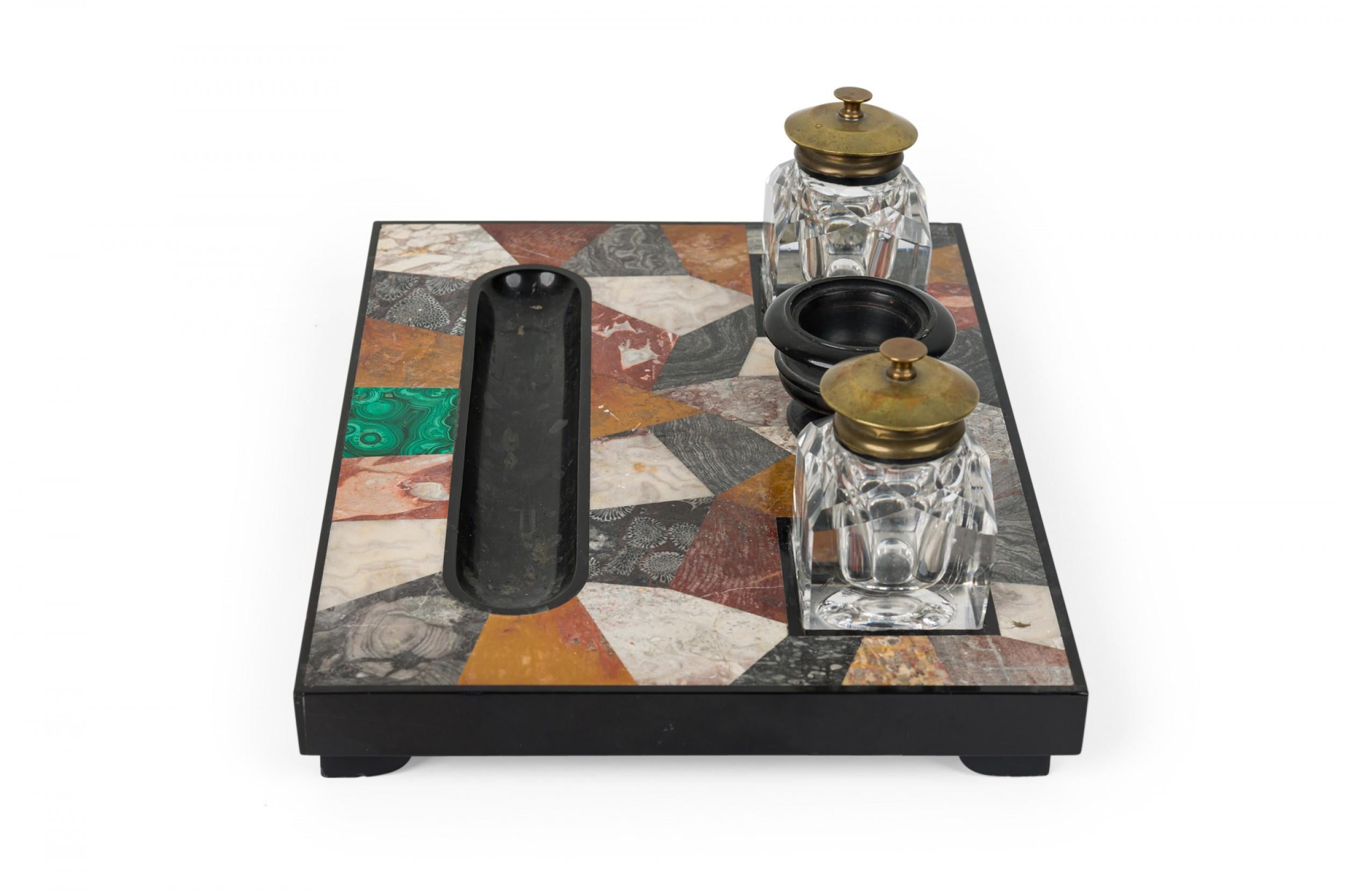 Calamaio inglese vittoriano (XIX secolo) con piede rettangolare composto da un mosaico di pietra dura intarsiato in un involucro di pietra nera intagliata. I calamai e il piedistallo sono realizzati in vetro sfaccettato con piani in ottone e
