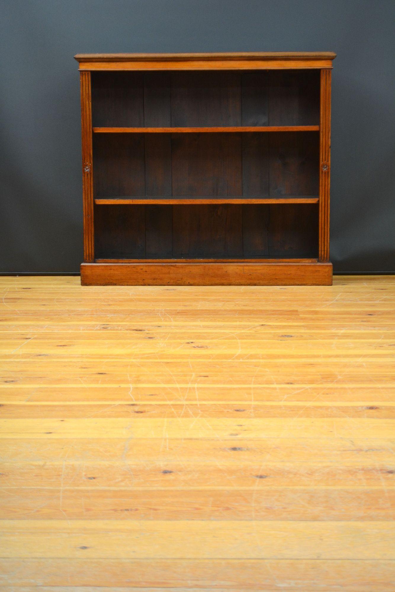 K0307 Late Victorian walnut open bookcase, having oversailing figured walnut top above two height adjustable shelves, flanked by fluted pilasters with floral rosette carvings, all standing on plinth base. This antique bookcase has been restored in