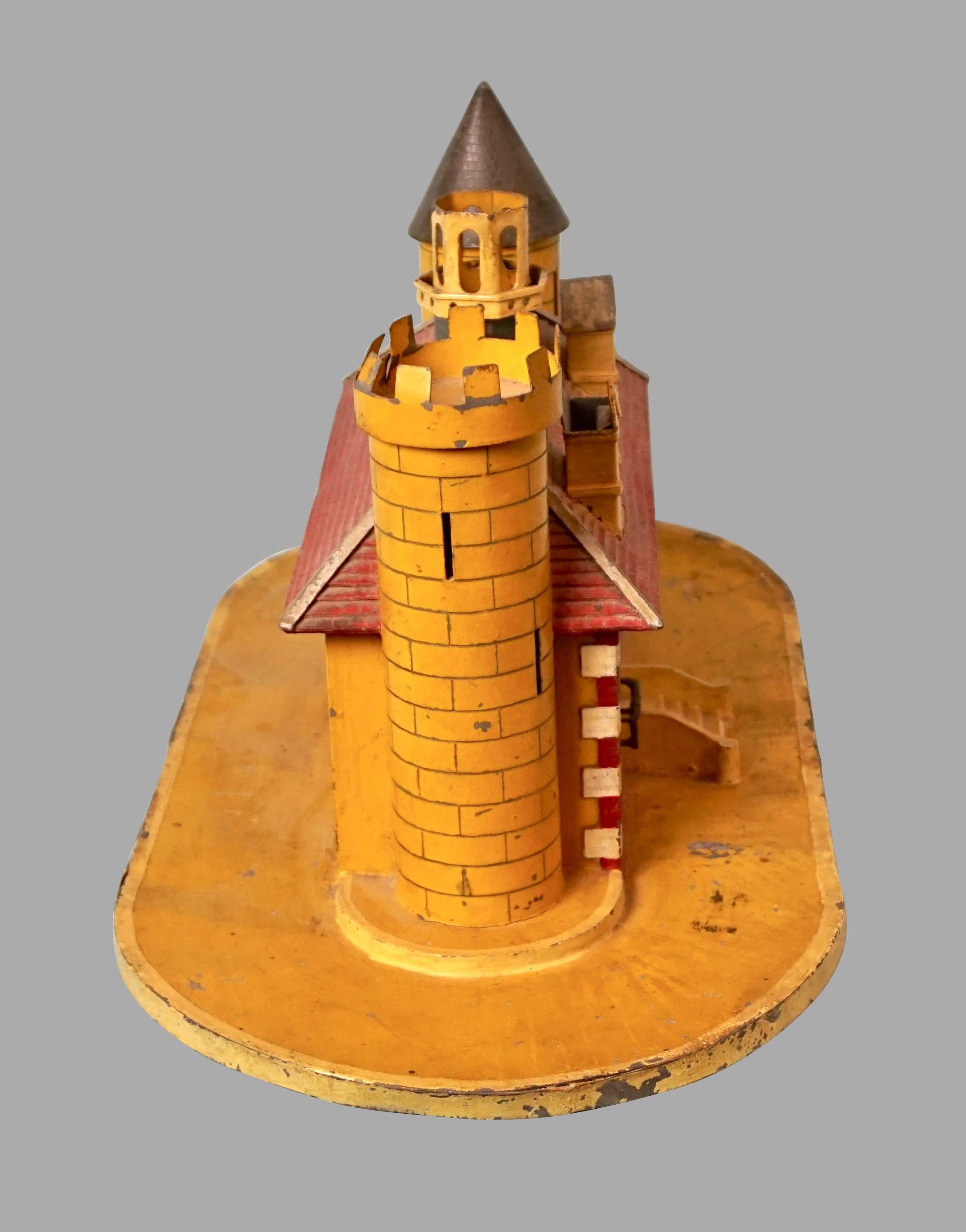 A charming English Victorian painted tin bank in the form of a castle, the turreted building painted in an array of bright colors with a peaked roof. Coins are retrievable from a slot in the bottom. Circa 1900.
