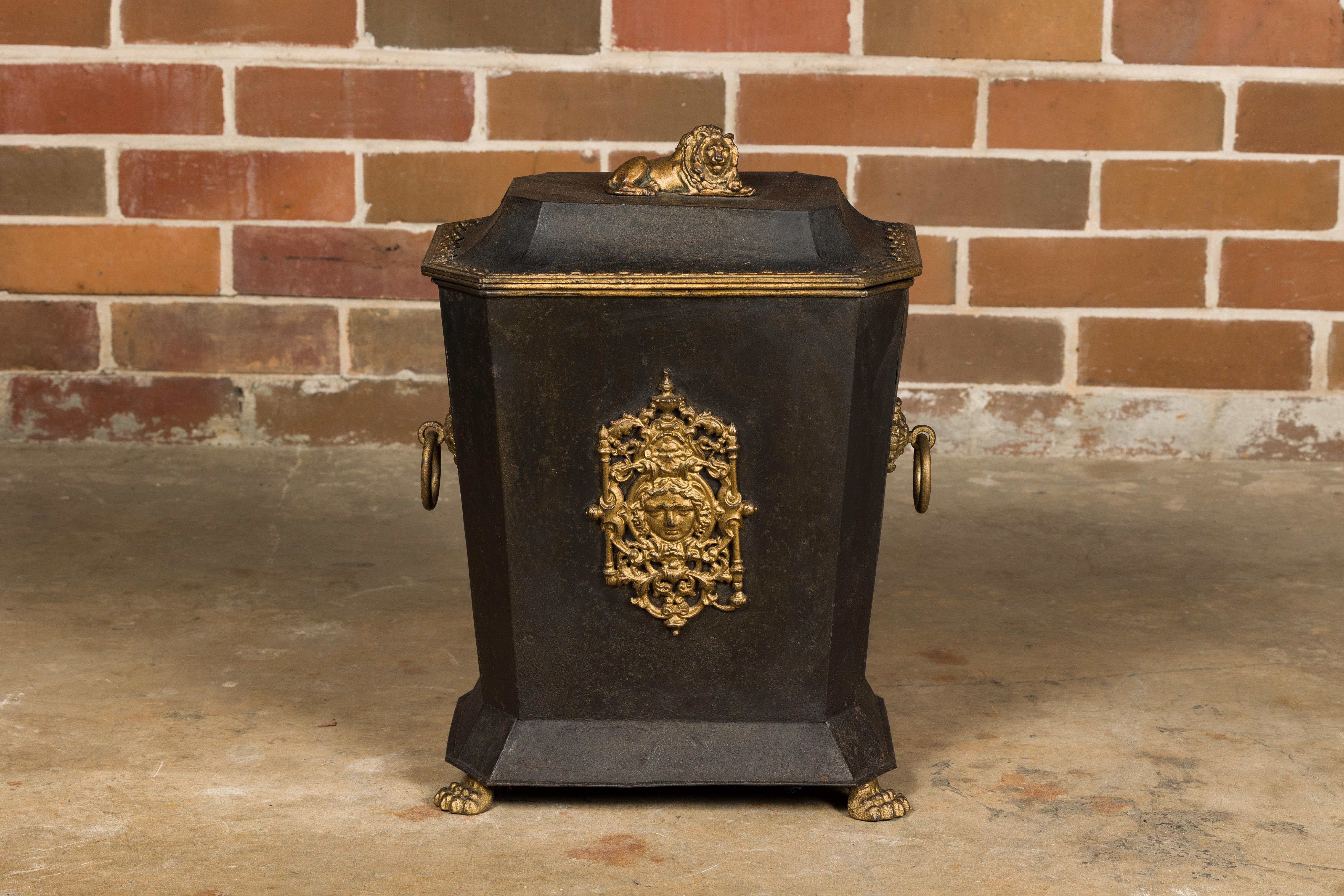 An English Victorian period black and gold tôle coal scuttle from the 19th century, with gilded lion and plate, lion paw feet and ring pull handles. Immerse yourself in the grandeur of the Victorian era with this exquisite English tôle coal scuttle,