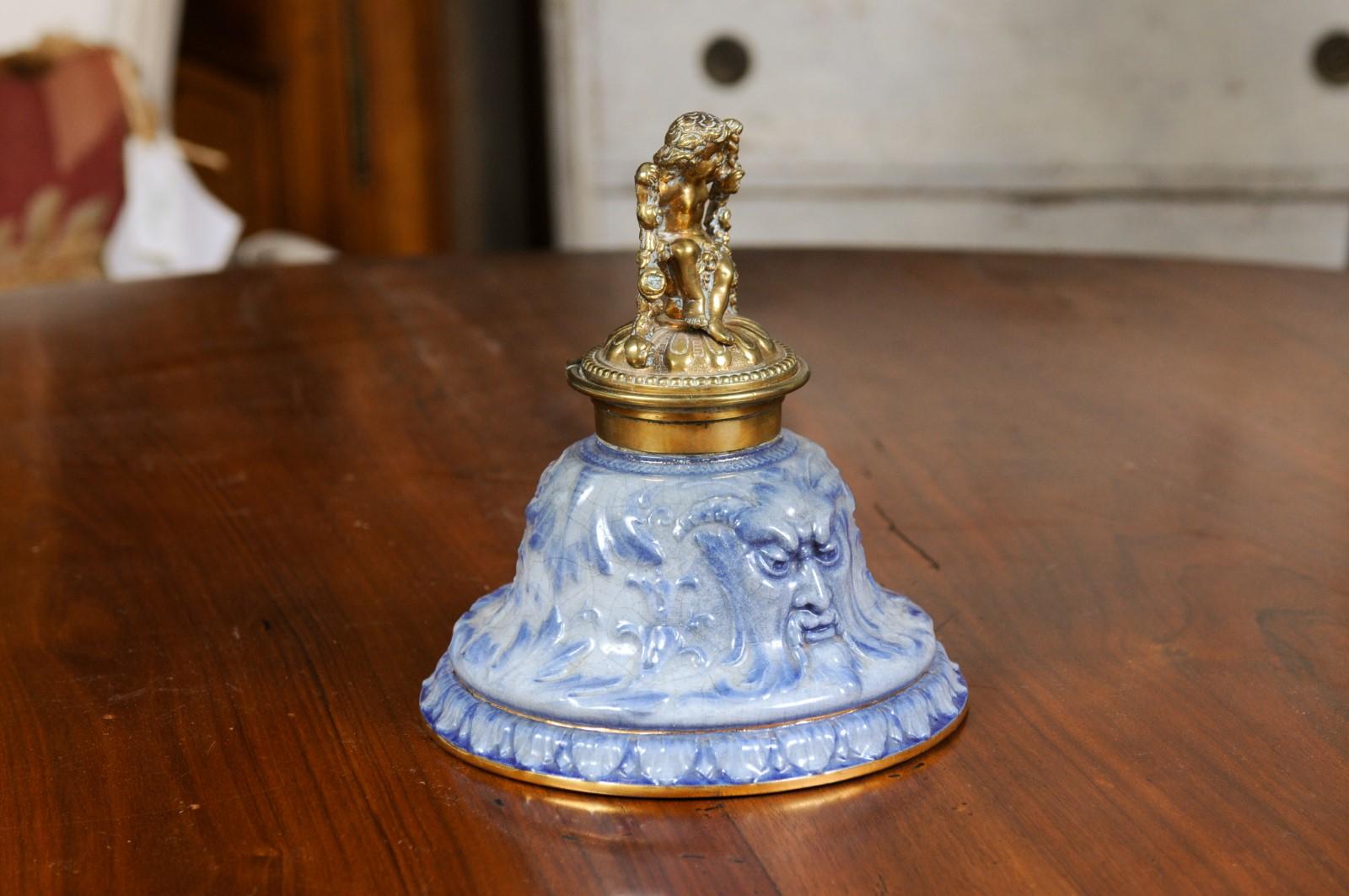 An English Victorian period porcelain and brass inkwell from the 19th century, with putto motif. Created in England during the Victorian era, this inkwell features a blue porcelain base adorned with satyrs and foliage motifs, topped with a handsome