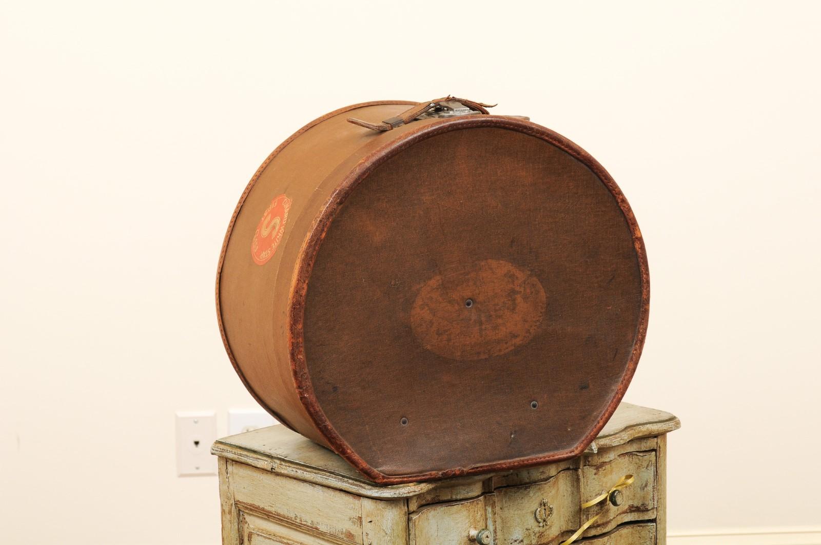An English Victorian period leather hat box from the mid-19th century, with first class sticker. Created in England during the reign of Queen Victoria, this leather hat box features a circular shape with a leather handle in the front and showcases a