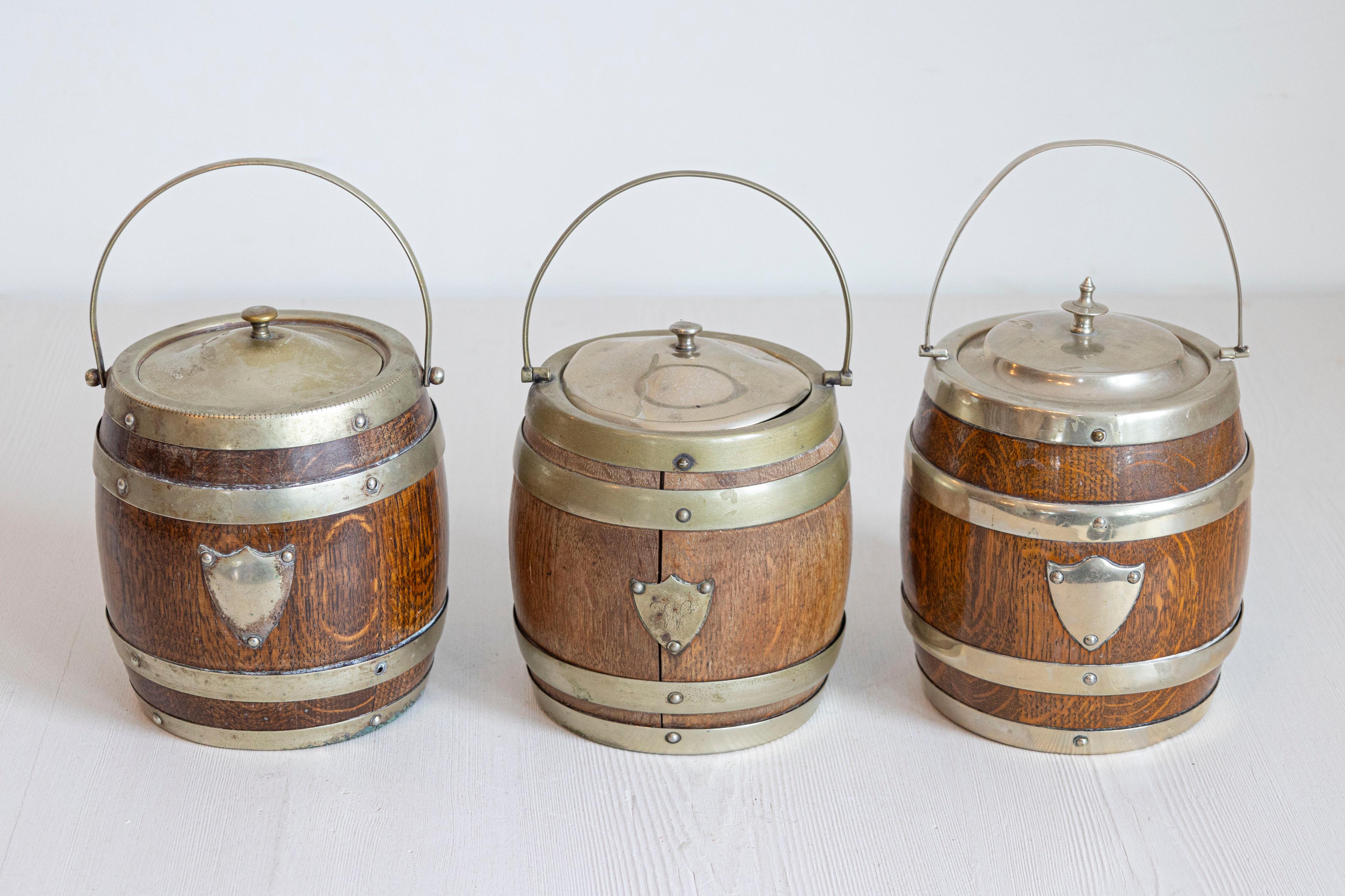 An English Victorian period oak lidded biscuit barrel from the late 19th century, with large handle and brass shield motif. We have currently three available, priced and sold $295 each. Created in England during the later years of the 19th century,