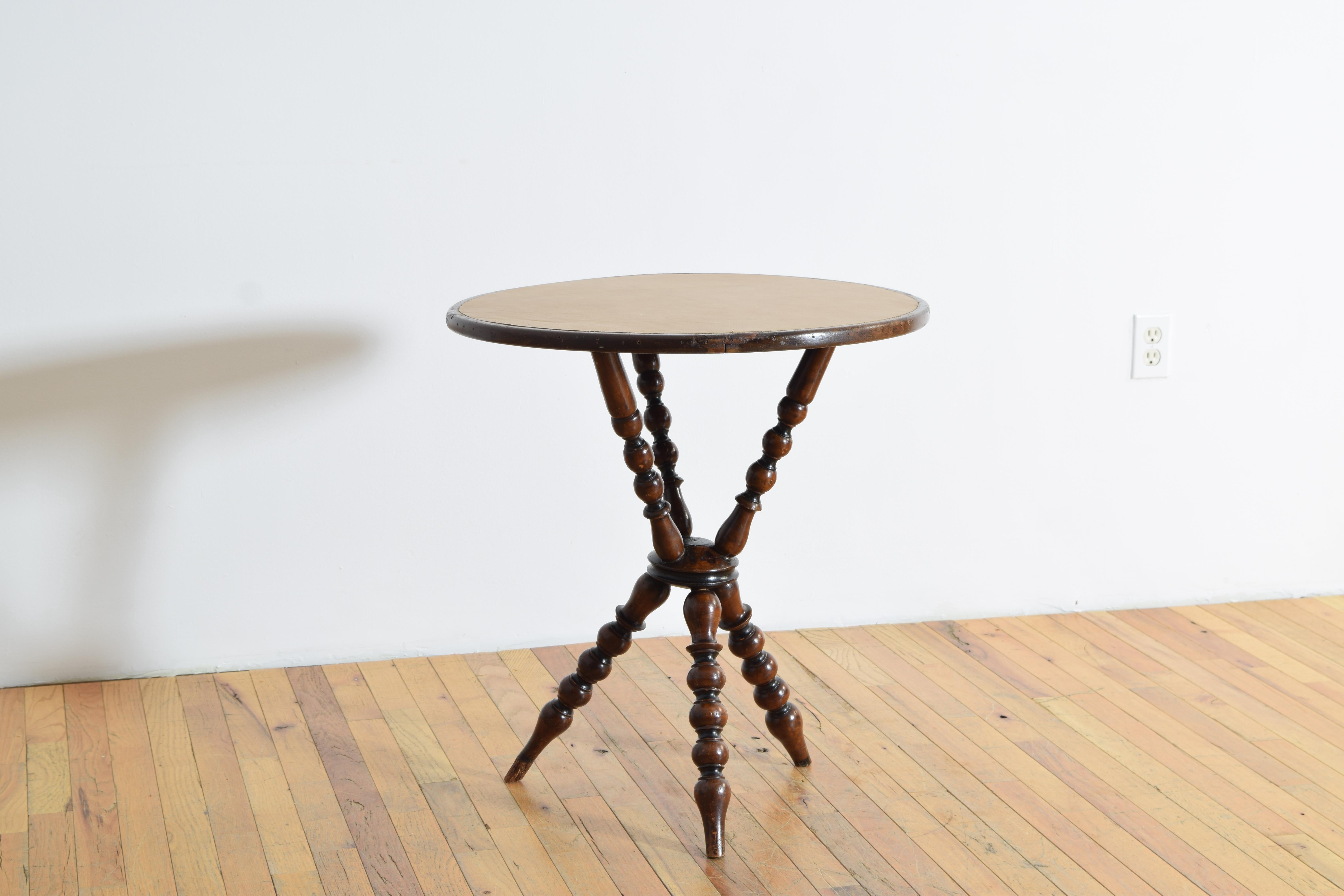 Plateau circulaire recouvert de cuir fauve clair, reposant sur trois pieds tournés se rejoignant au centre et se prolongeant vers le haut pour soutenir le plateau.