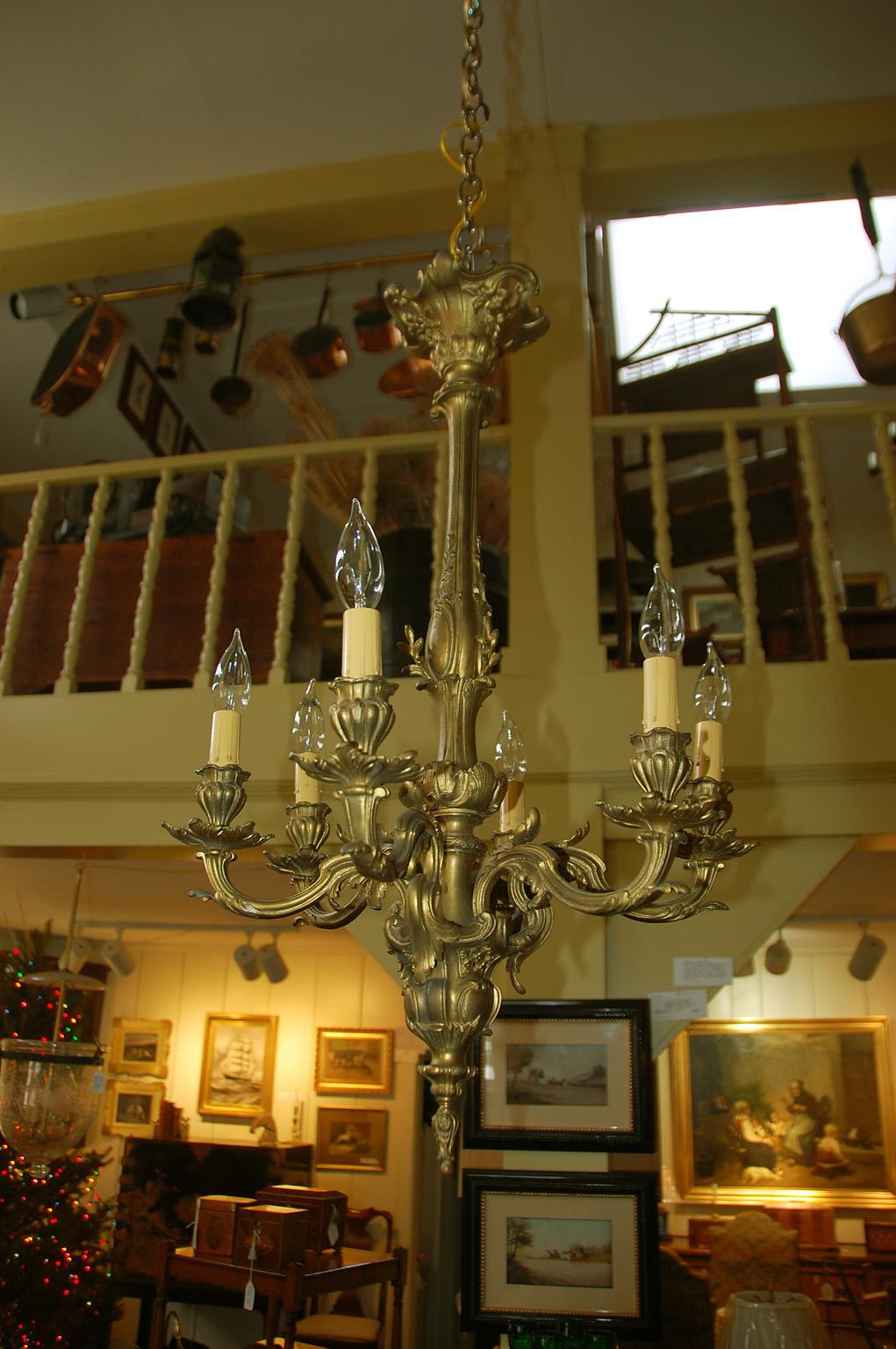 English Victorian rococo chandelier in gilded cast bronze with six arms. This medium sized chandelier has a recurring theme of acanthus leaves. Acanthus leaves appear in the arms, the drip pans, the candle cups and on the central stem and ball. This