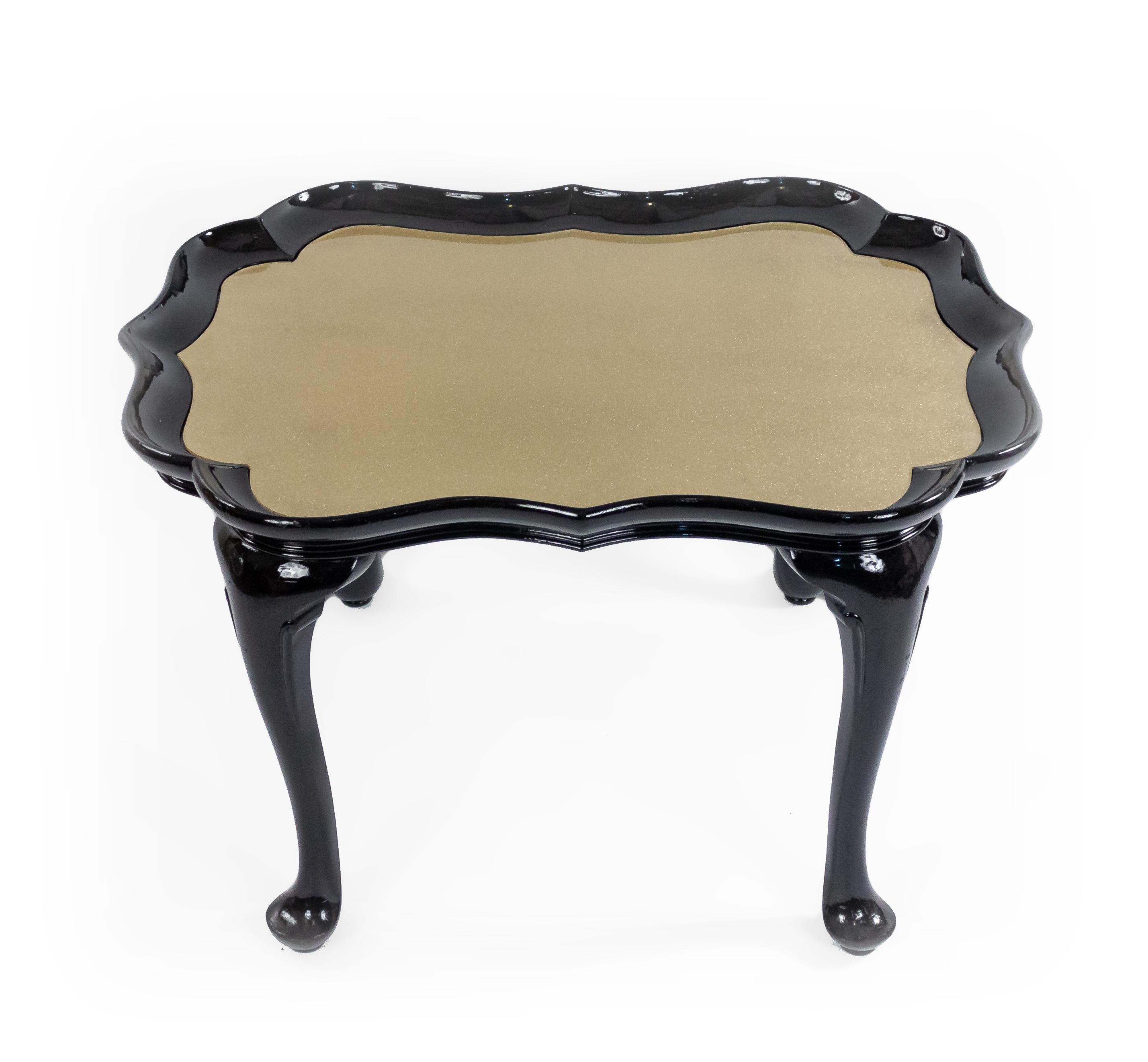 English Victorian-style coffee table with a scalloped gold plexiglass inset top resting in an ebonized Queen Anne-style base.
