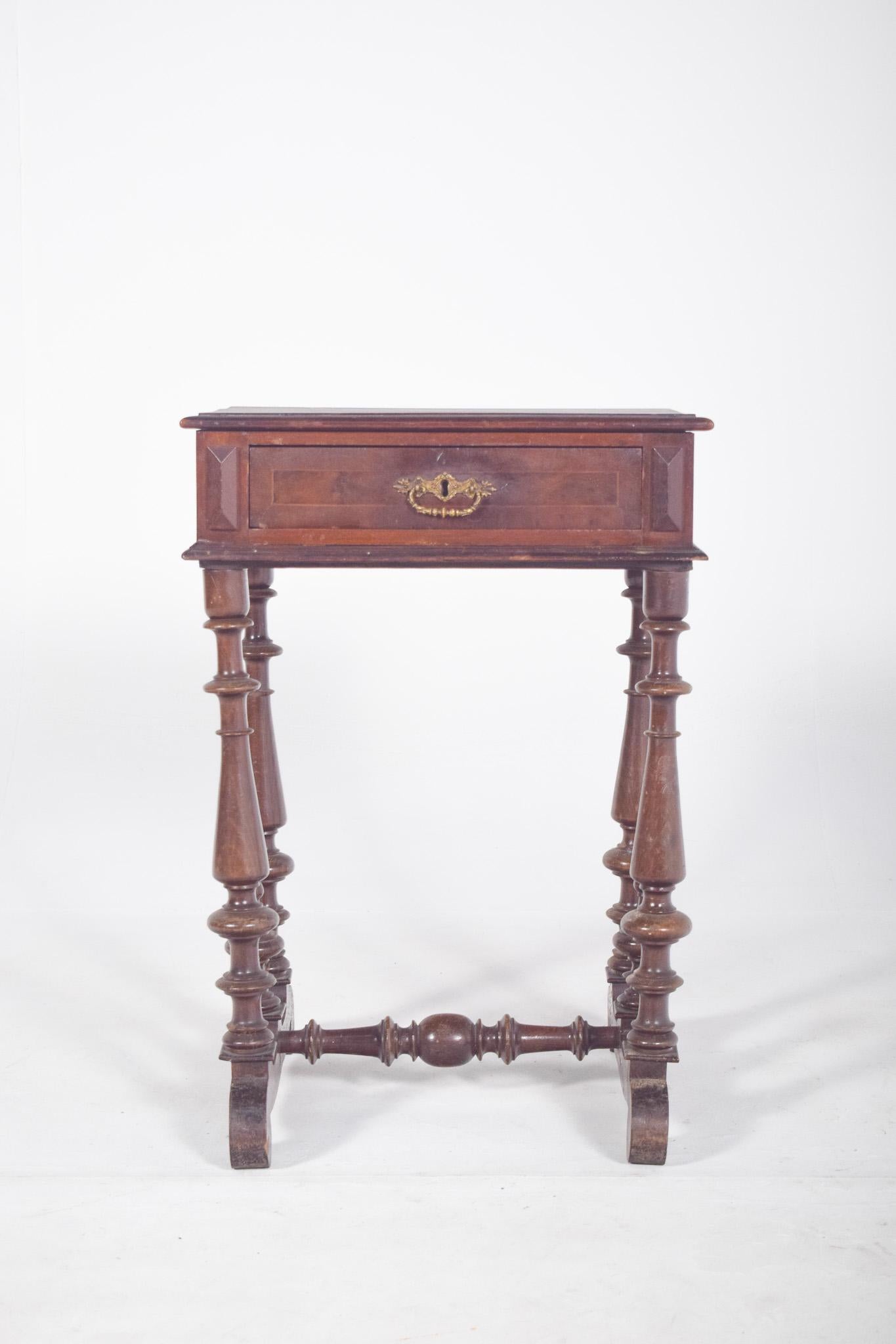 Sewing table with one drawer. Rectangular top with moulded edges and one front drawer with metal handle, drawer panel decorated with carved fillet. With four turned legs with tapered profiles and ring elements, connected by horizontal braces and two