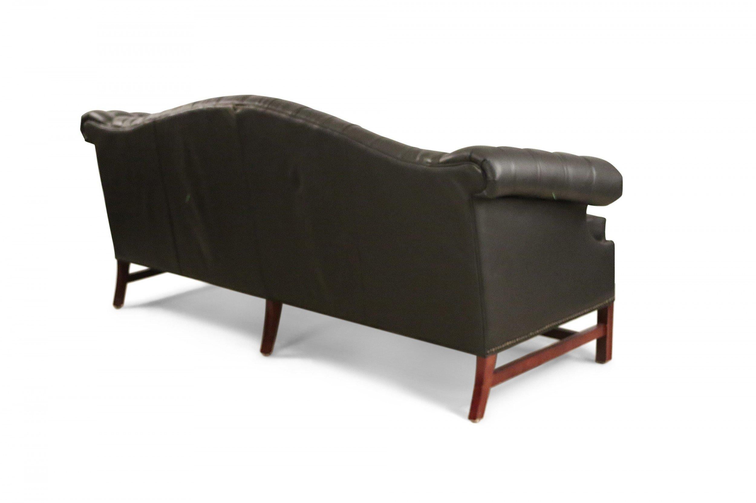 English Victorian-style (20th Century) three-seat camel back design sofa with black button tufted faux-leather upholstery and brass nail head detail with a wooden stretcher and legs, and a single seat cushion.
 