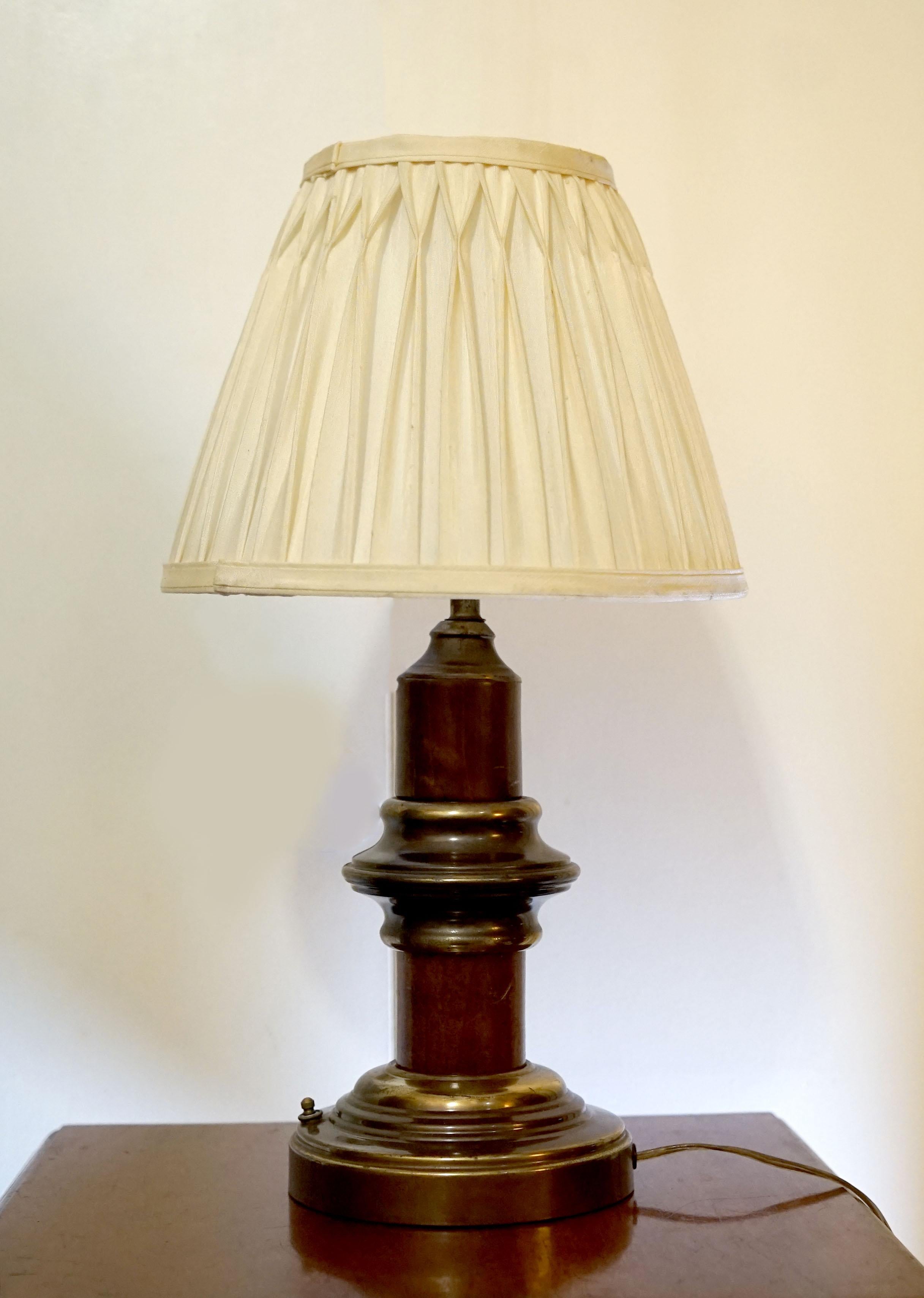 The contrast of deep wood tones and the brass base and middle section give this lamp a finished look. The brass patina is developed. This victorian style desk lamp is attractive for its compact form and original pinch-pleat lampshade among other
