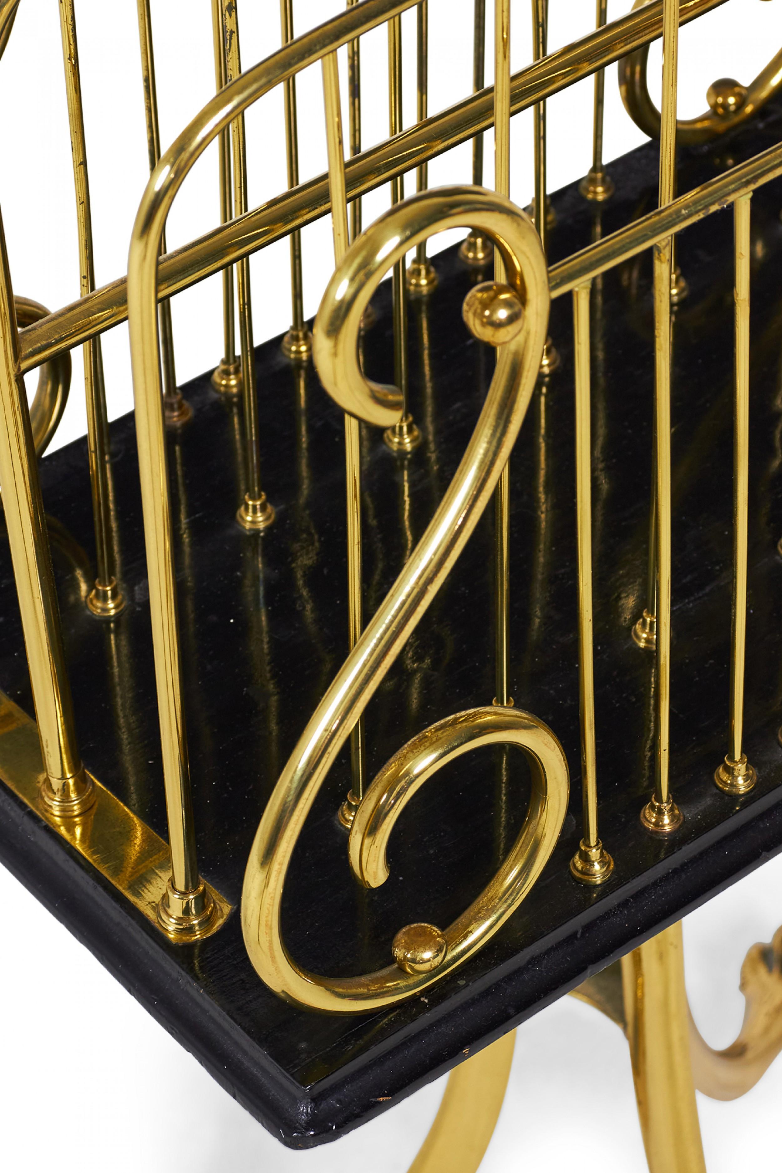 Revistero/librero inglés de latón, de estilo victoriano, con parte superior en forma de lira de cuatro secciones, suelo de madera lacada en negro, apoyado en una base de pedestal con soporte central lacado en negro rodeado de tres patas de latón