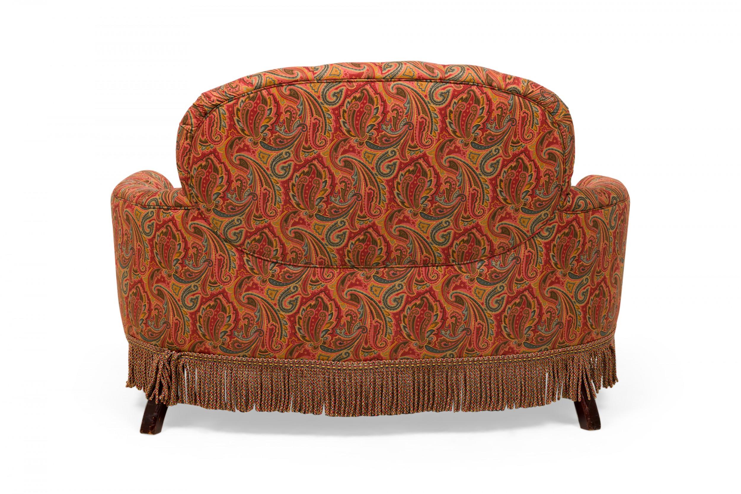 Causeuse anglaise de style victorien à dossier arrondi, accoudoirs incurvés et assise en forme, tapissée d'un tissu paisley rouge, orange, jaune et bleu avec détails touffus et bord plissé, reposant sur quatre pieds en bois tourné avec une jupe à