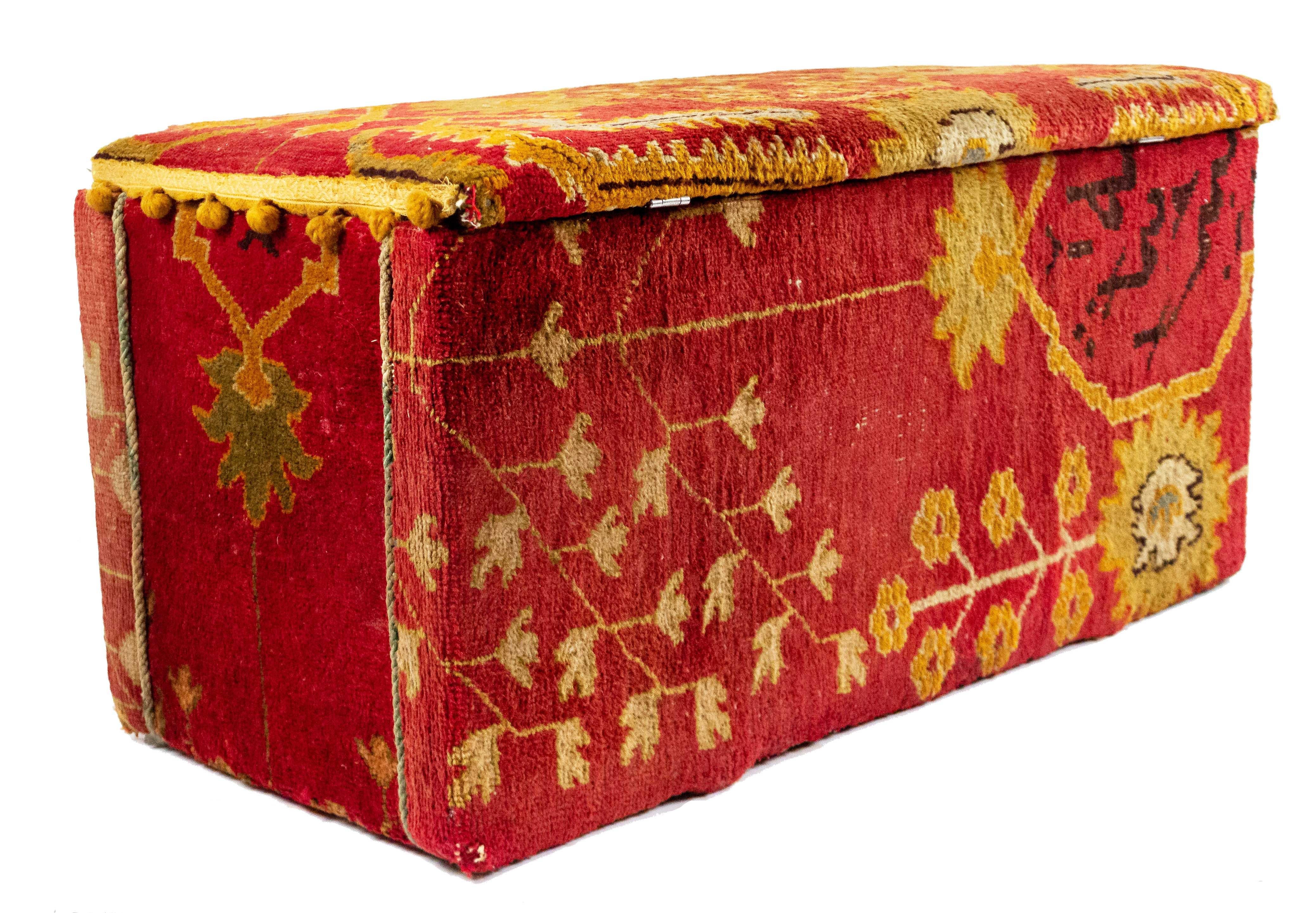 English Victorian style Turkish carpet upholstered floor trunk with red, green, and yellow design.