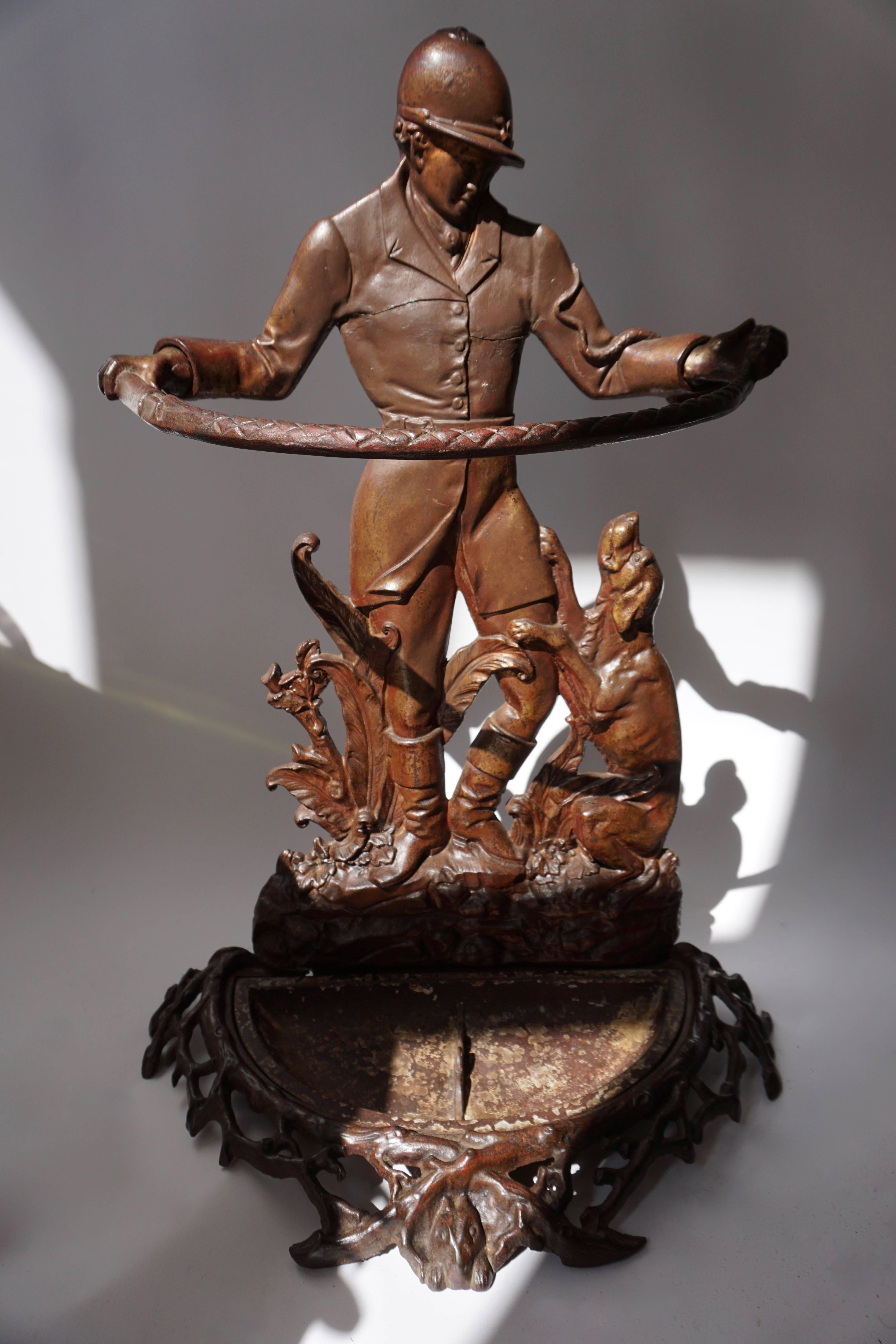 An unusual and inventive cast iron English Victorian umbrella stand representing  a hunter with his dog, holding a whip to form the cane holder, standing amidst the greenery on a rocky soil, the base shaped as underwood with a hiding rabbit in the
